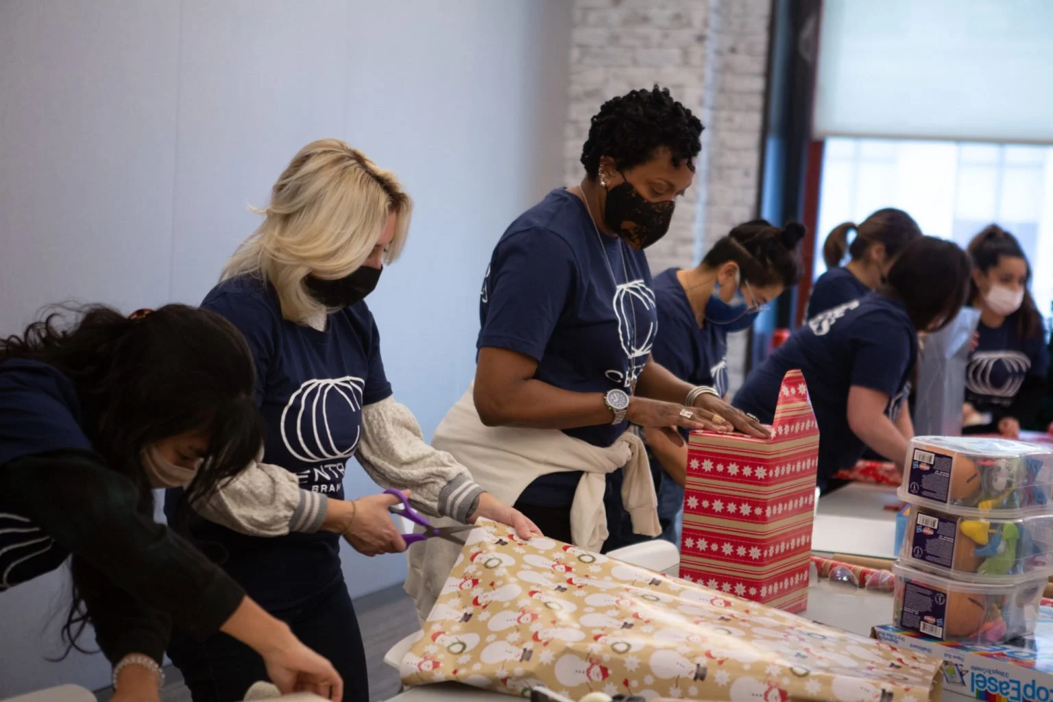 People wearing masks wrapping Christmas presents at a table.