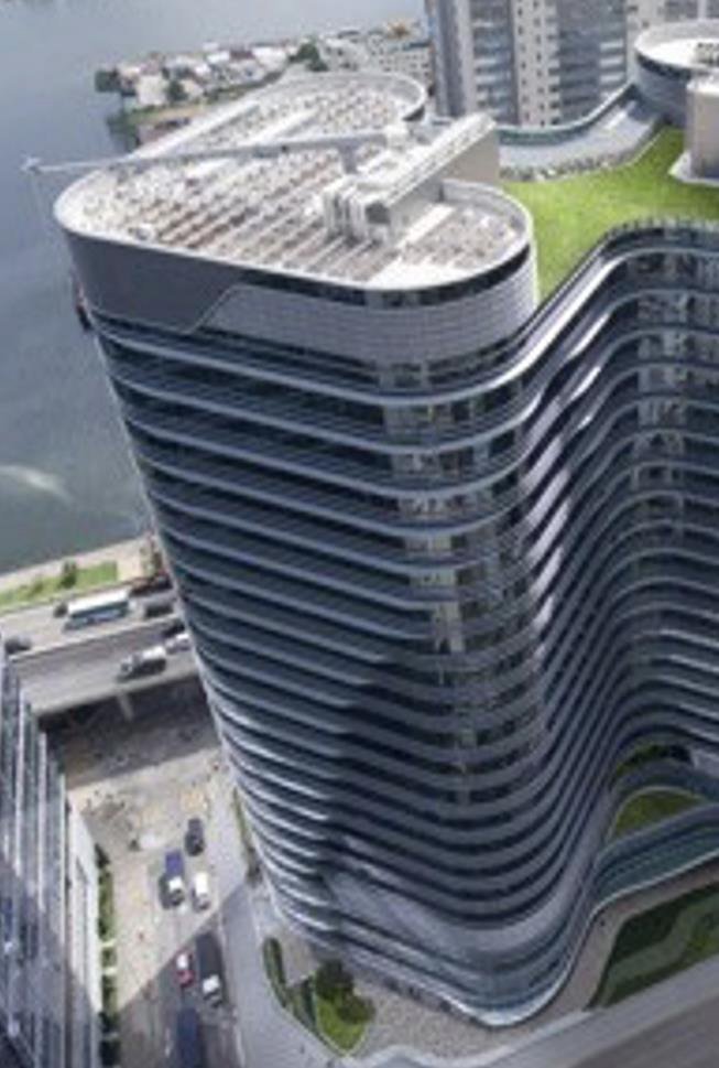 A tall modern building with curved, layered architecture, green rooftop area, and a street with cars below.