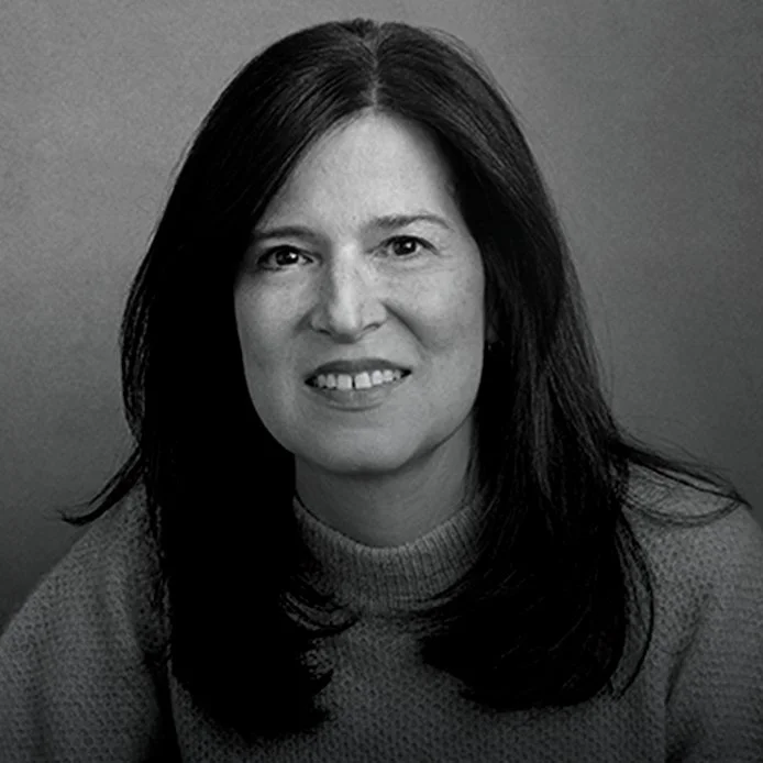 Black and white portrait of a woman with shoulder-length dark hair, smiling and wearing a knit sweater, against a plain background.