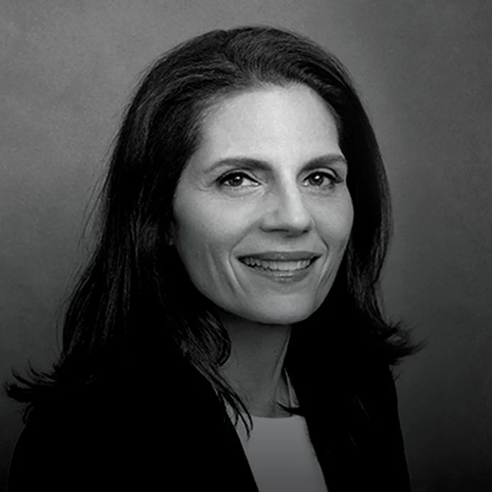 Black and white portrait of a woman with shoulder-length dark hair, smiling, against a plain background.