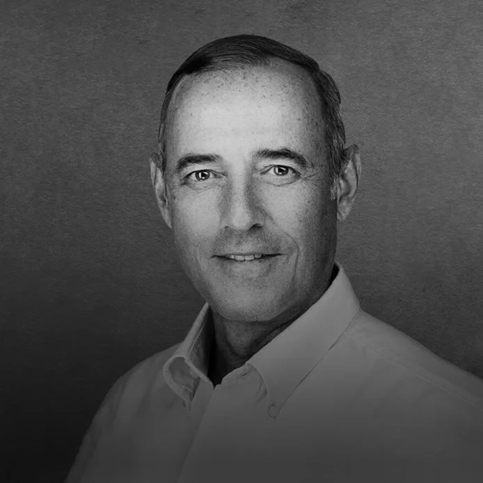 Black and white portrait of a middle-aged man with short dark hair, wearing a collared shirt, smiling softly, against a plain background.