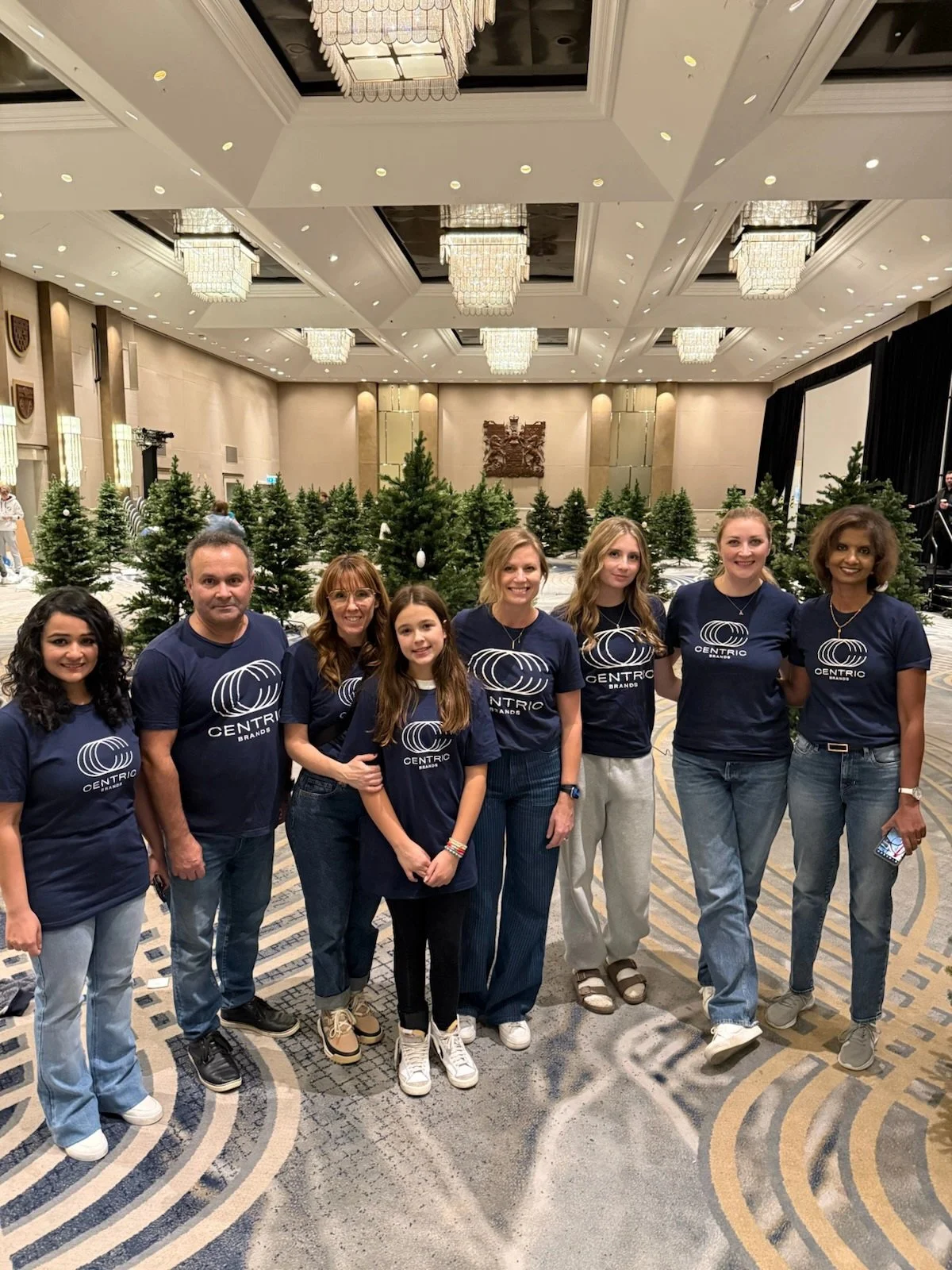 Group of eight people posing together in a decorated conference room with Christmas trees and chandeliers.