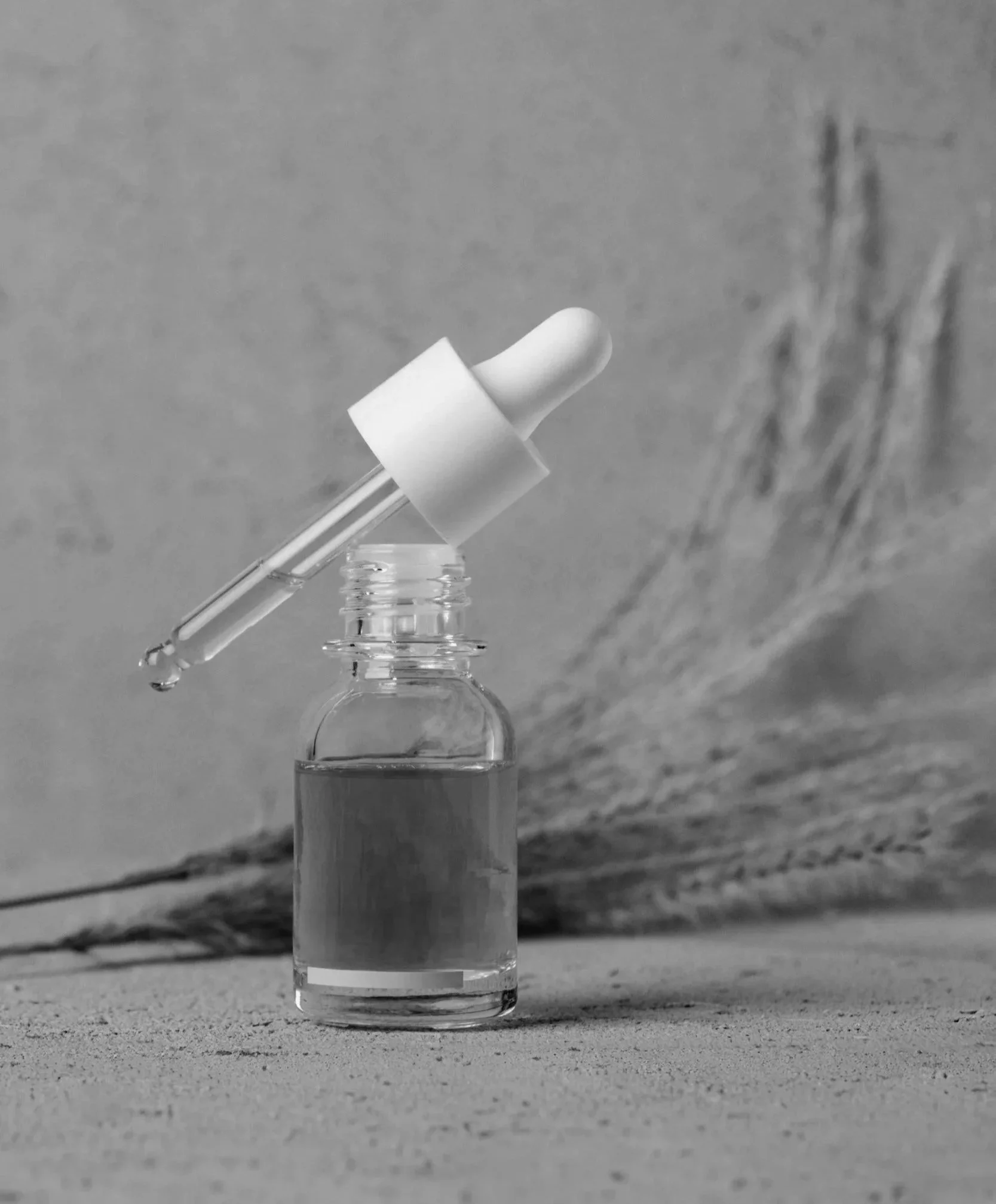A small glass bottle with a dropper cap containing a liquid, placed on a textured surface with a blurred textured background.