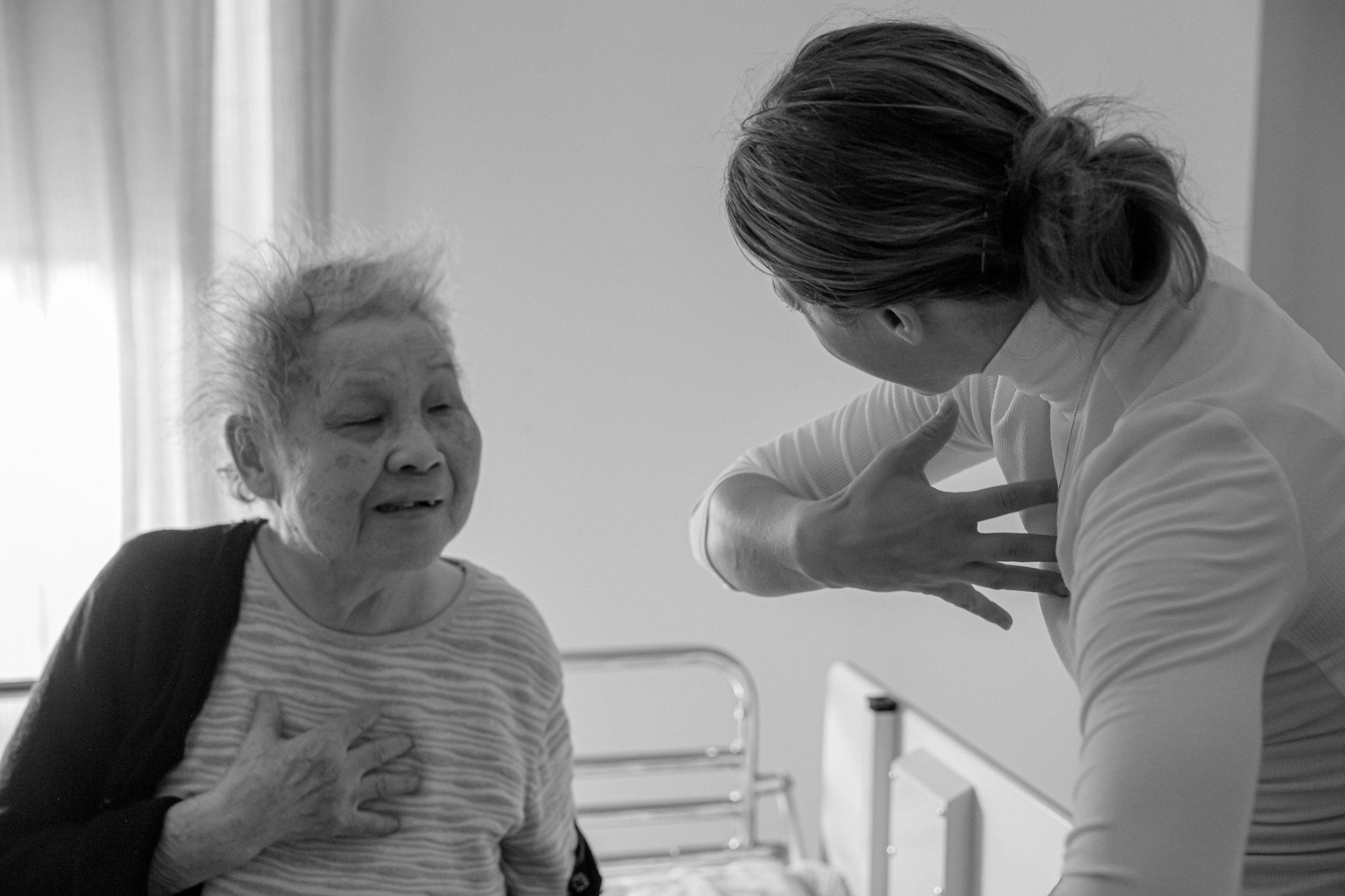 Une infirmière parle avec une femme âgée dans une chambre d'hôpital, la femme âgée a la main sur la poitrine et semble exprimer de la détresse.
