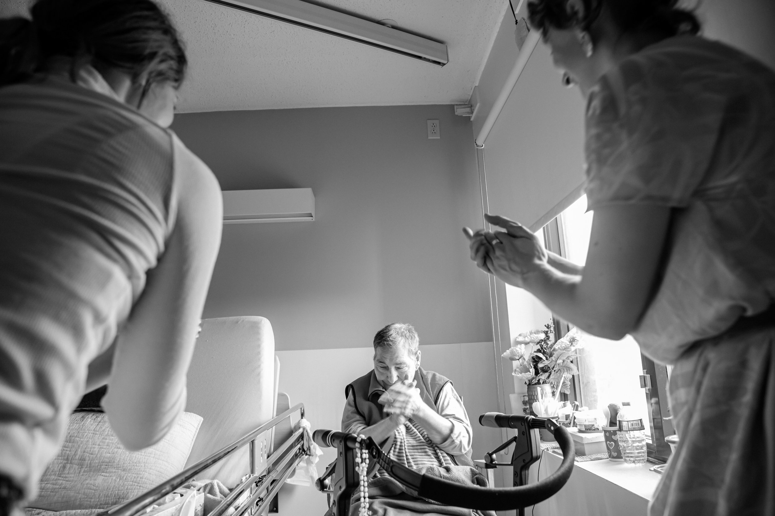 Une scène dans une salle d'hôpital montrant une personne allongée dans un lit, entourée de deux autres personnes en vêtements de soin. La personne dans le lit semble attentive à ce que la personne à gauche lui dit ou fait, dans un environnement éclai