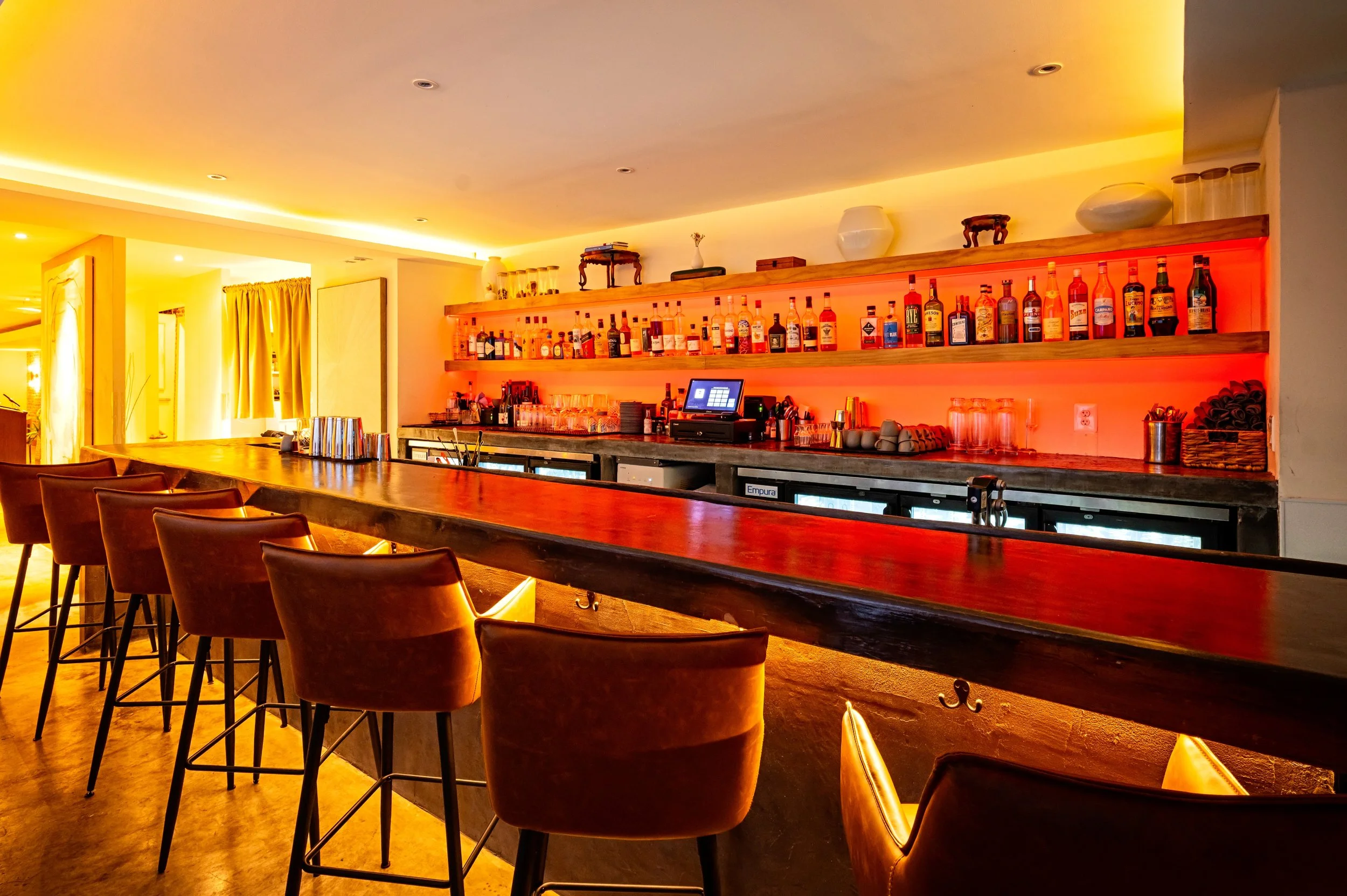 Empty bar with leather chairs and illuminated shelves with various liquor bottles.