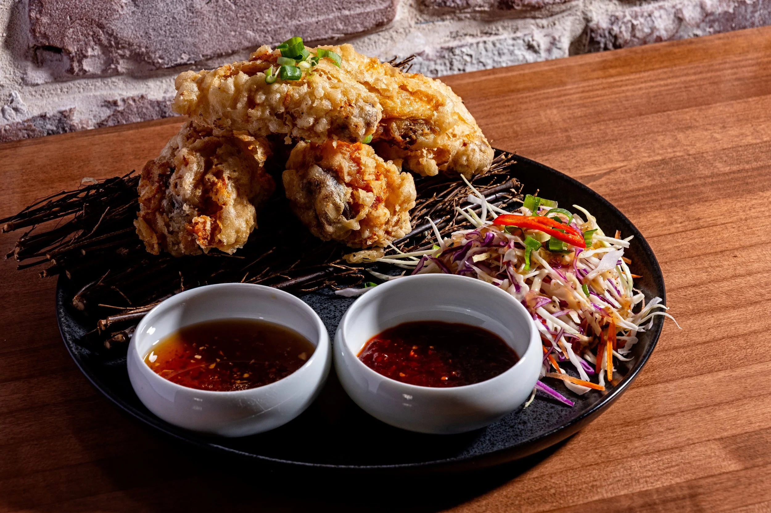 Fried chicken with two dipping sauces, shredded cabbage salad, and chopped green onions on a black plate.