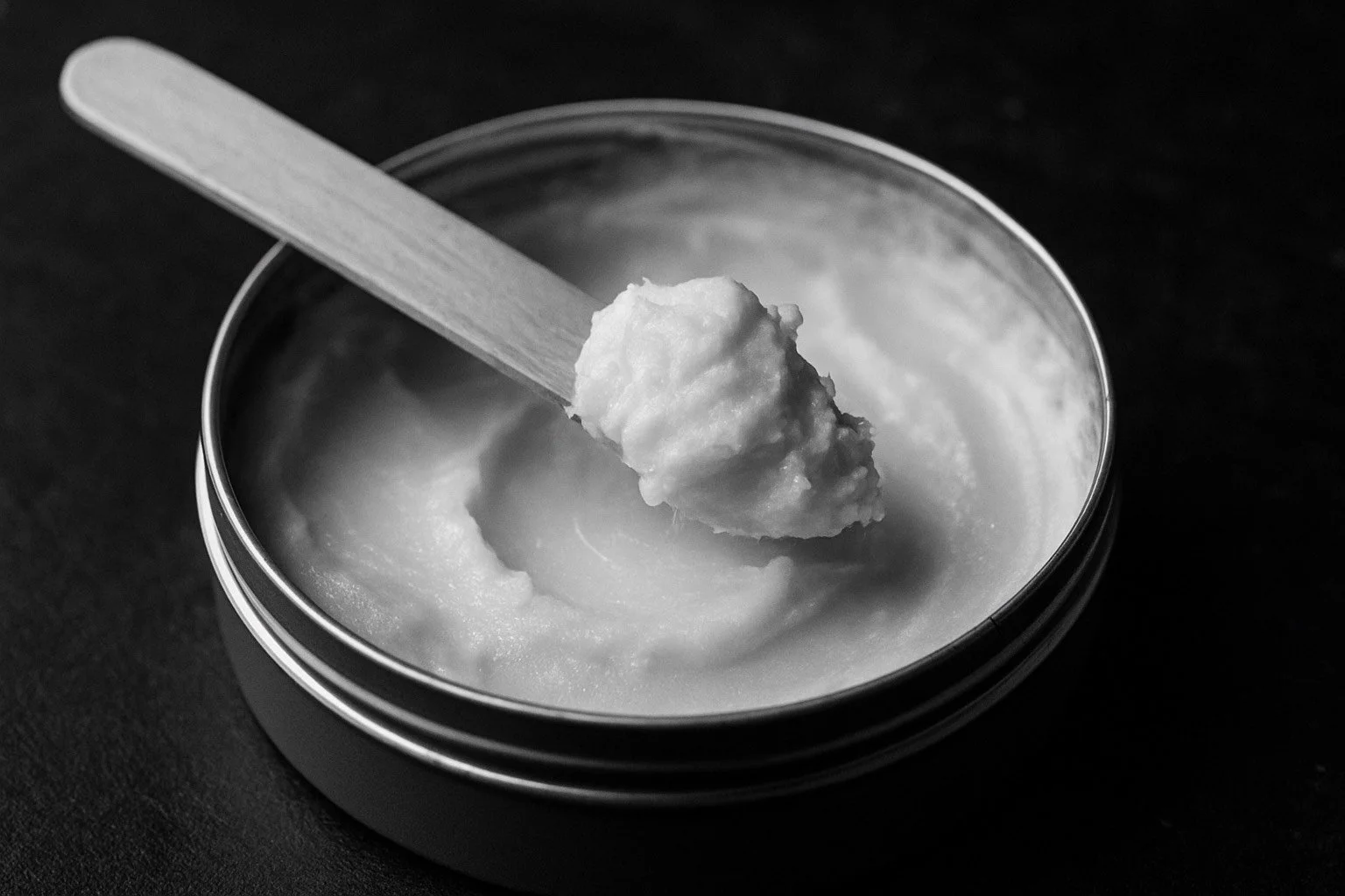 Black-and-white photo of a tin can filled with a creamy substance, with a wooden spatula holding a scoop of it.