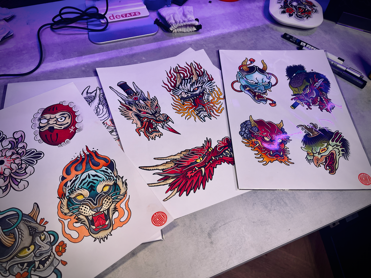 Hand-drawn tattoo flash sheets laid out on a studio table