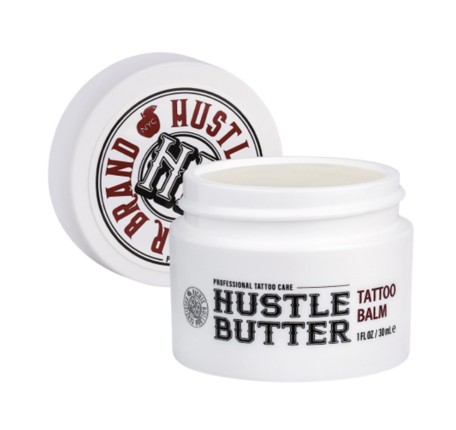 A white jar of Hustle Butter tattoo balm with an open lid showing the balm inside.
