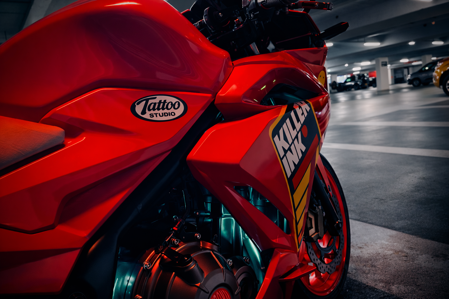 Close-up of a red sport motorcycle parked in a parking garage, featuring a Tattoo Studio sticker and Killah Ink decal on the fairing.