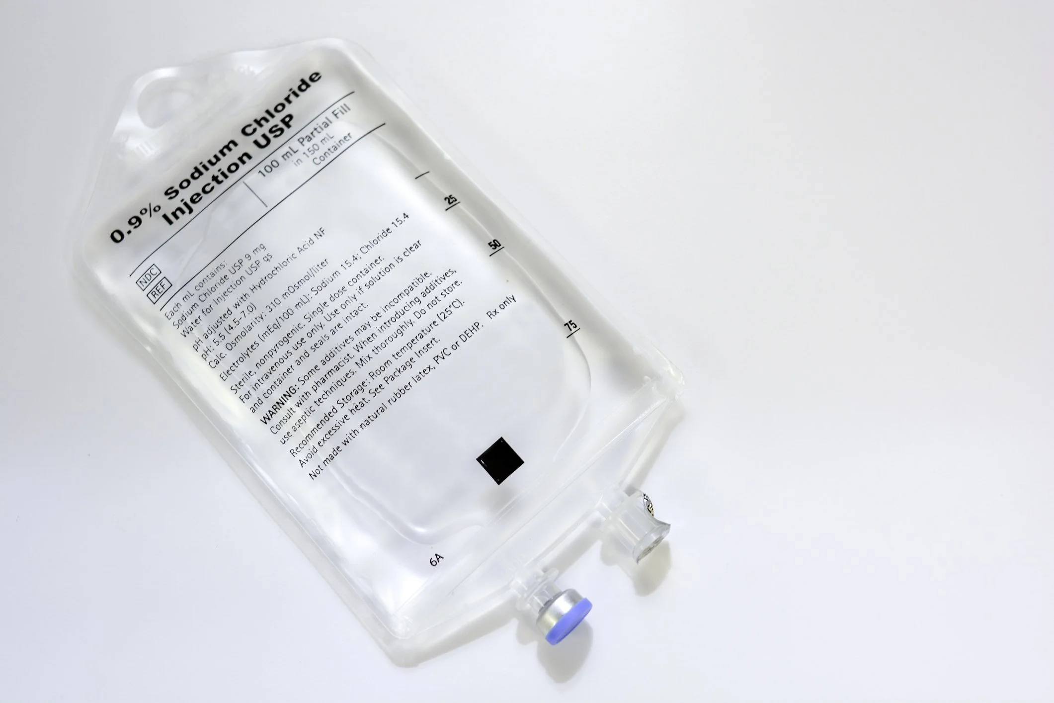 A clear plastic bag with a label indicating it contains 0.9% Sodium Chloride injection. The bag has a blue cap and a plastic tube at the bottom, placed on a light surface.