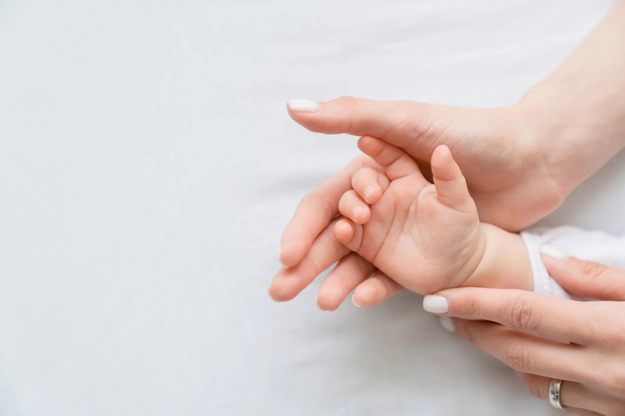 Close-up of an adult's hand gently holding a baby's hand against a white background.