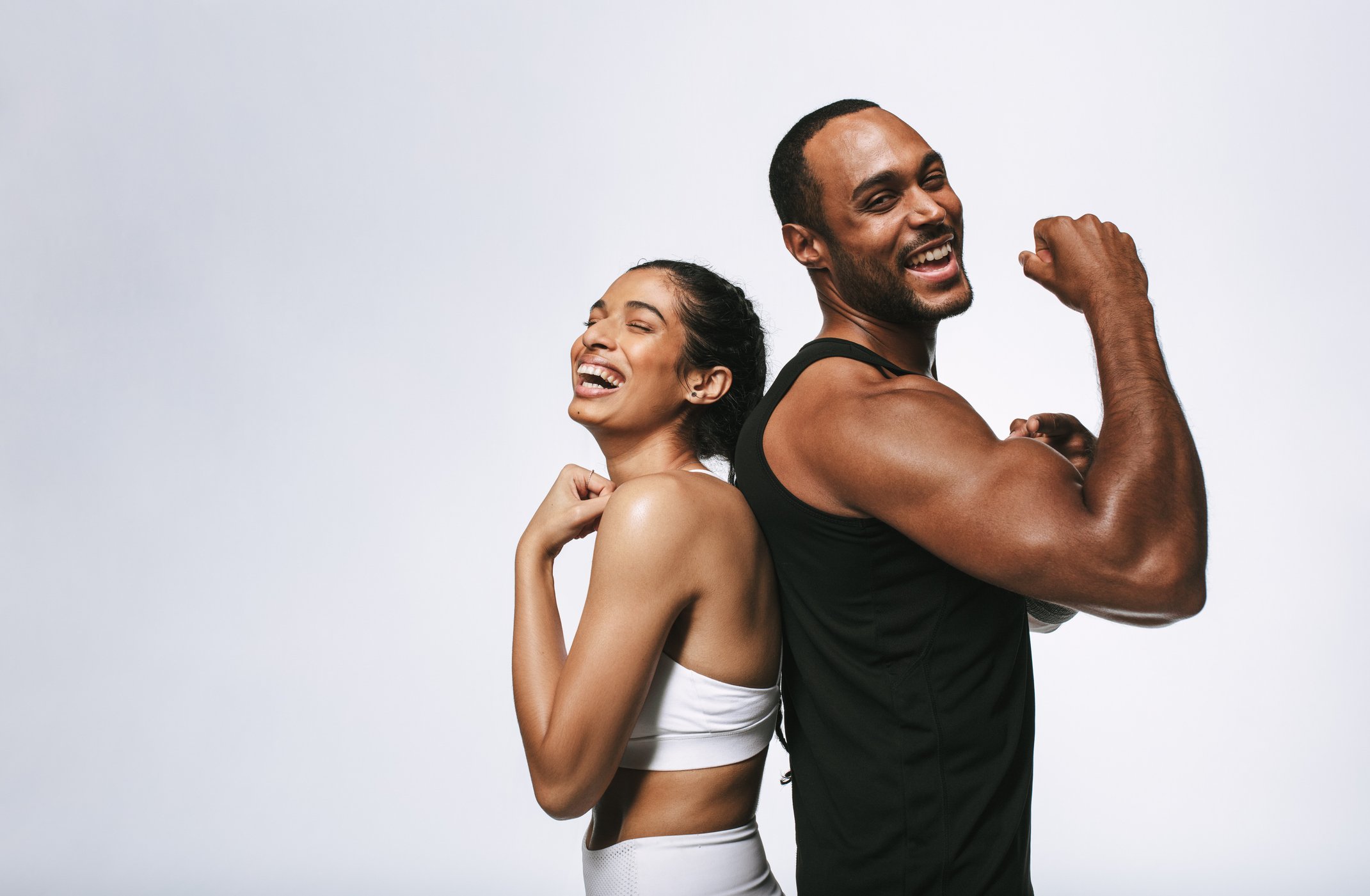 A happy woman and man standing back-to-back, smiling and displaying strength with flexed arms, against a plain white background.