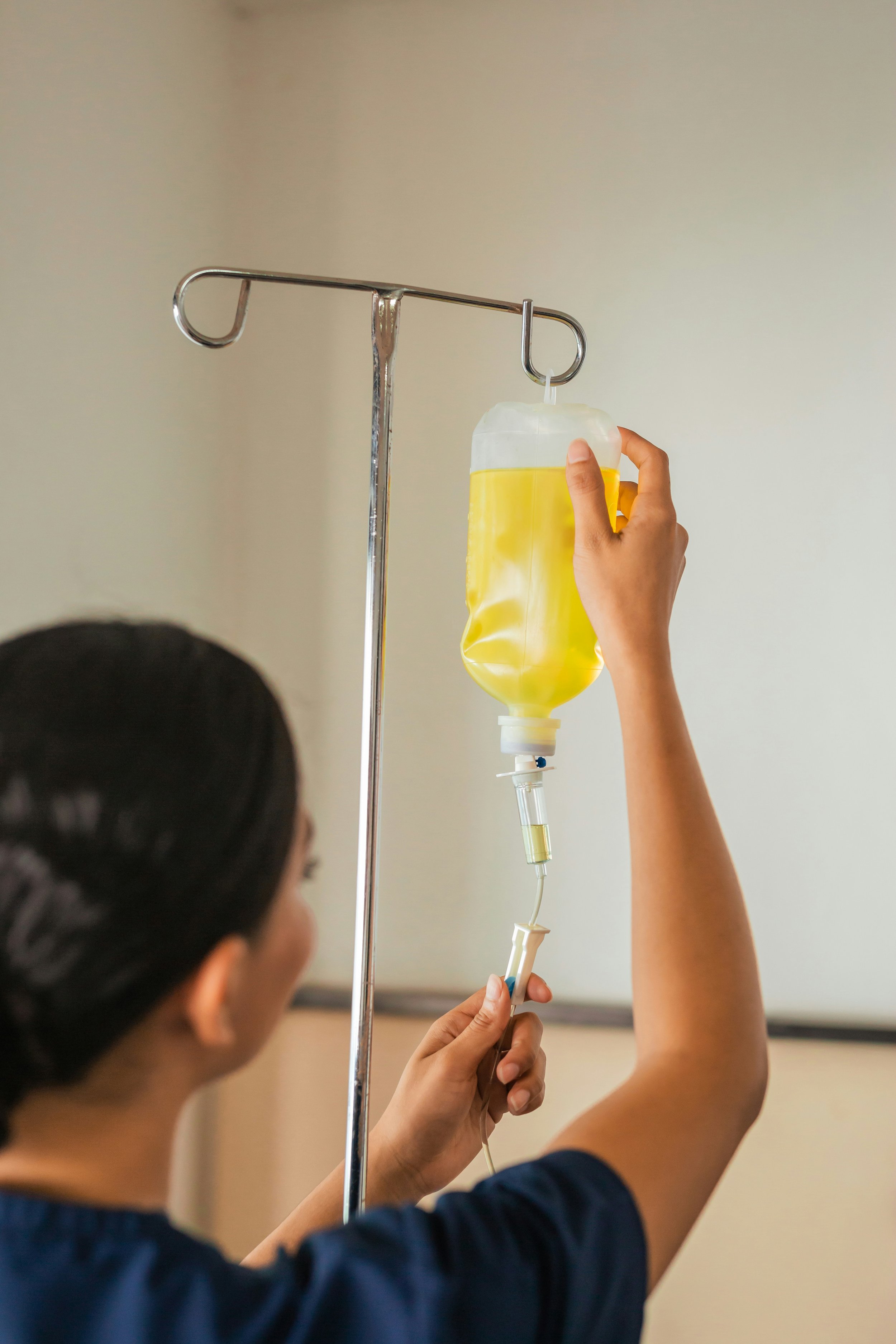 A person adjusting an IV bag filled with yellow liquid hanging on a stand in a medical setting.