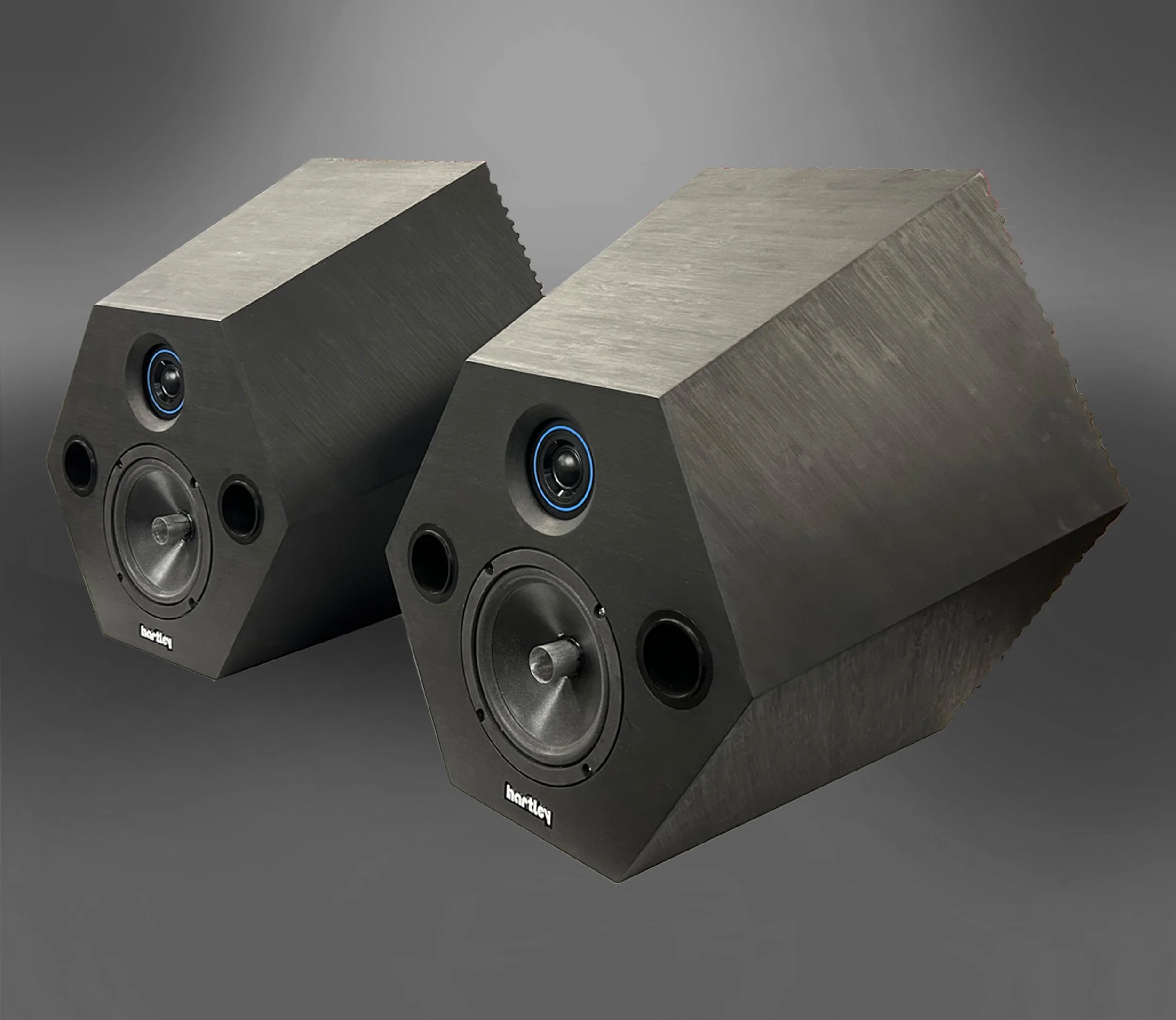 Two black bookshelf speakers with a trapezoidal shape, featuring multiple drivers, against a gray background.