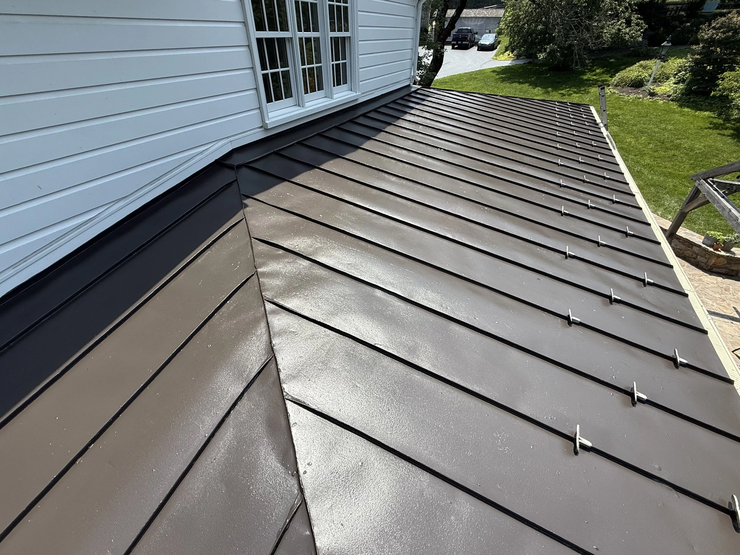 Metal roof with black panels on a suburban house, shown from above during daytime.