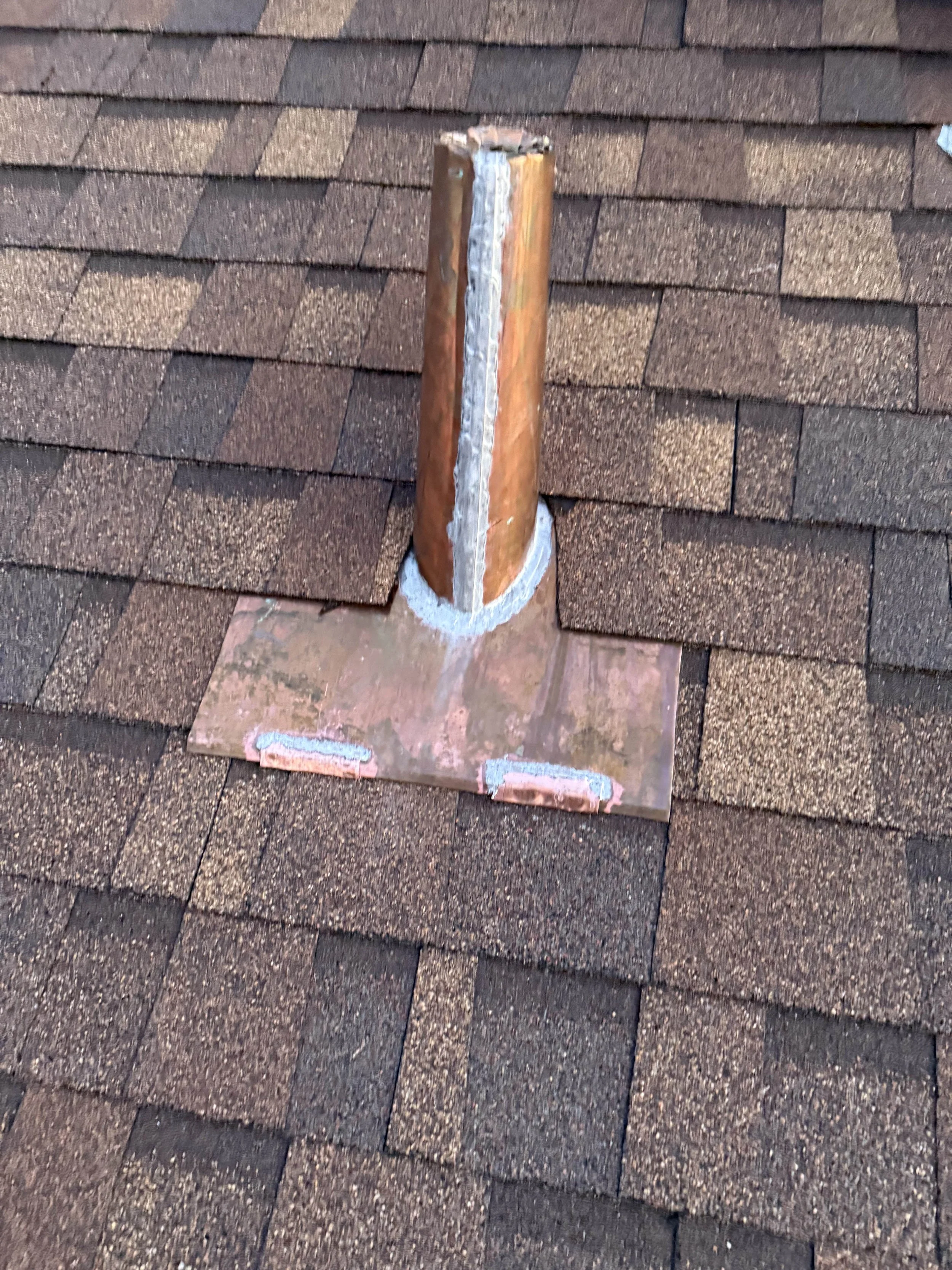 Copper pipe flashing installed on a brown asphalt shingle roof, ensuring proper waterproofing and leak protection.