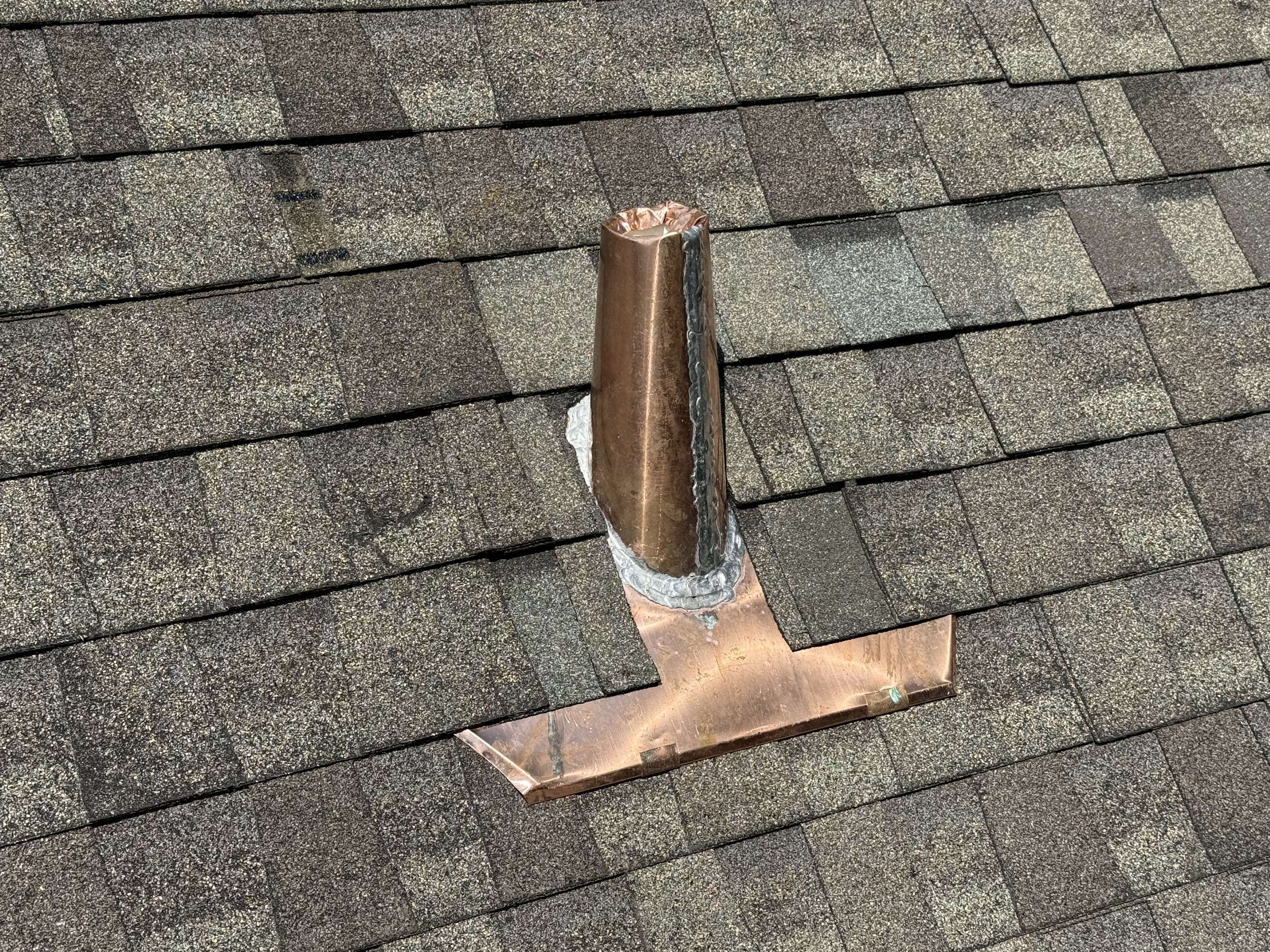 Close-up of a roof vent pipe with a copper flashing on asphalt shingles.