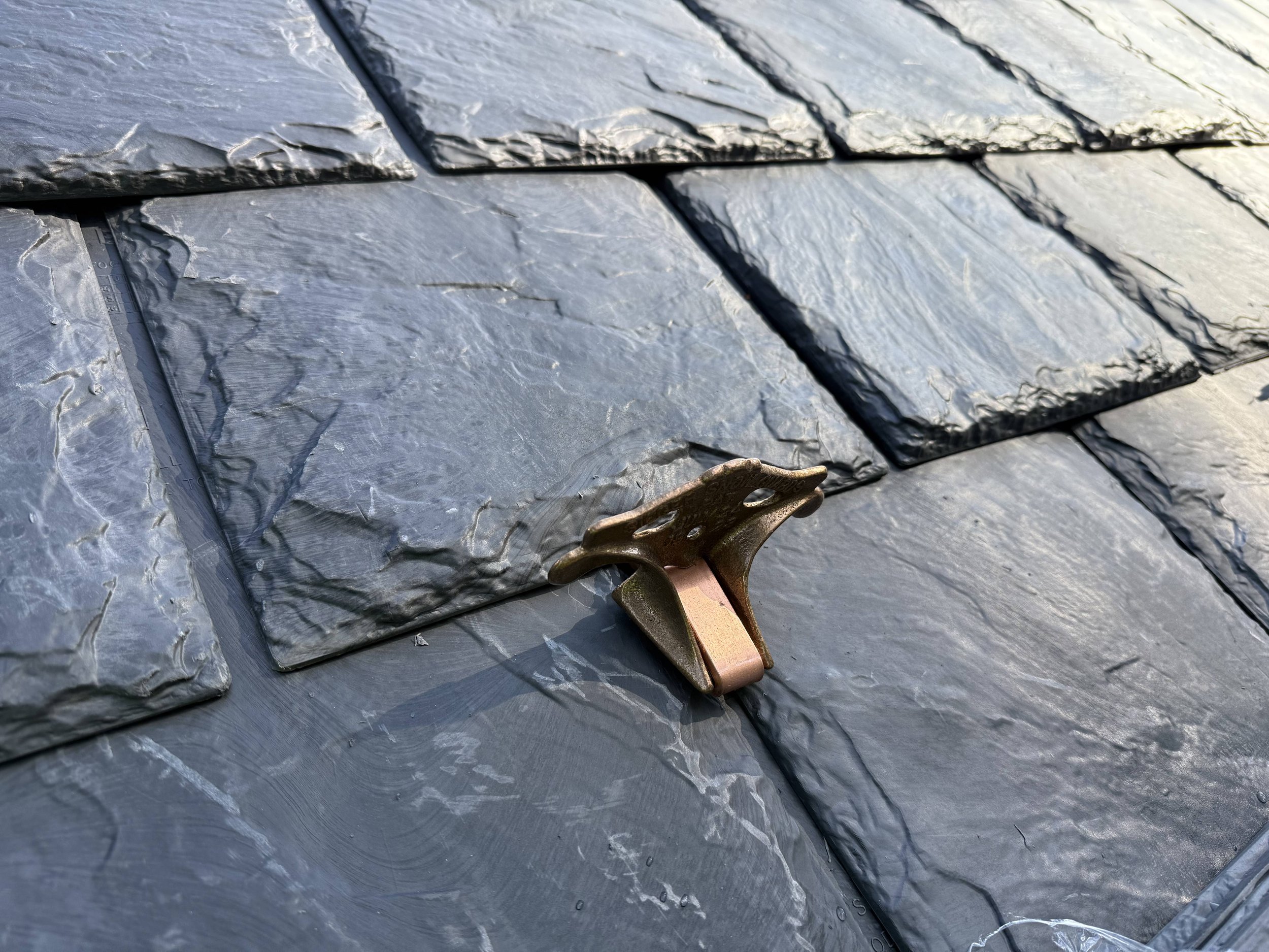Close-up of slate shingles on a roof, with a copper-colored roof clip holding them in place.