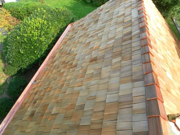 Close-up view of a cedar shingle roof with trees and grass in the background Chester County PA.