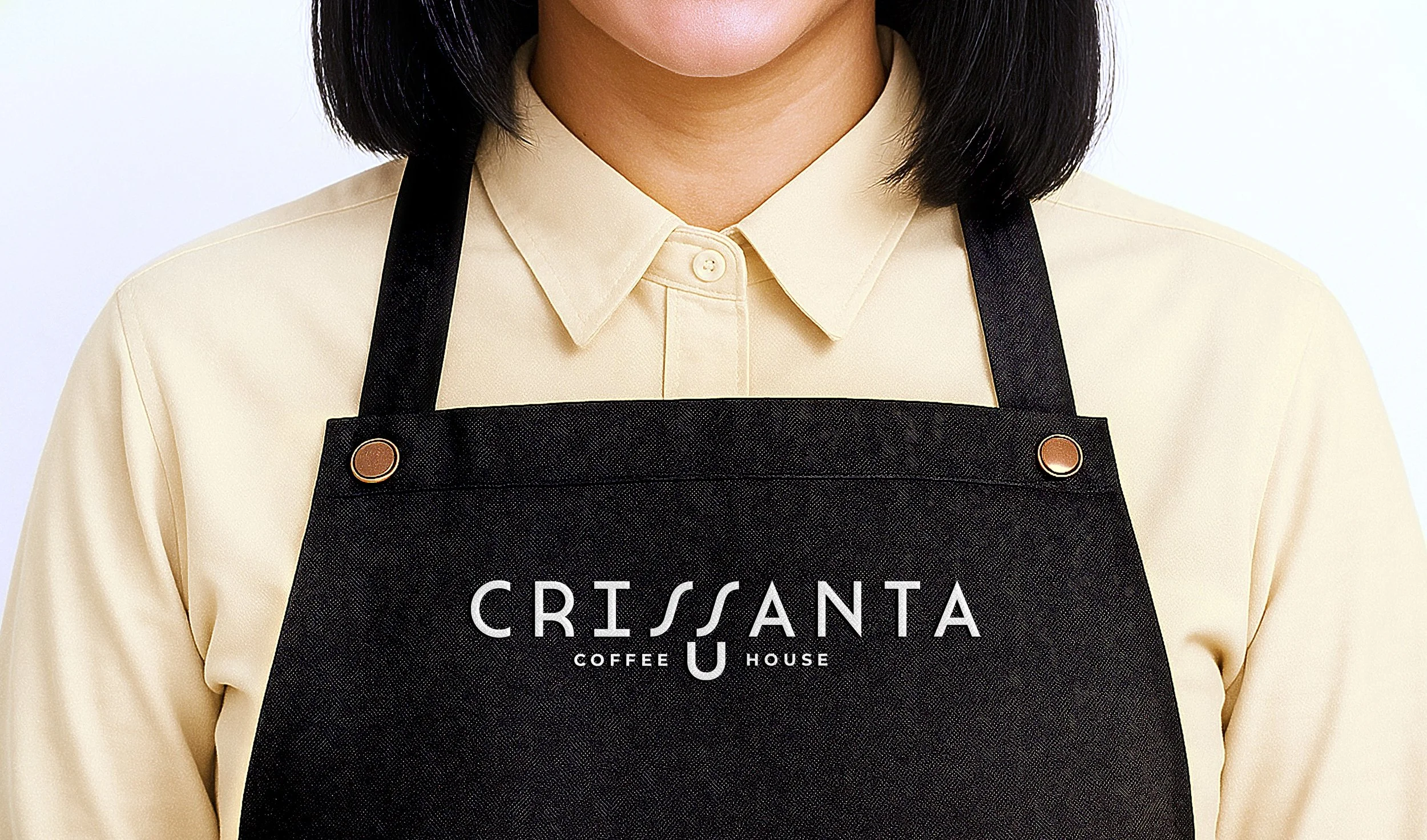 Close-up of Crissanta Coffee House barista uniform with branded black apron and beige shirt, showcasing modern coffee shop identity and professional attire.