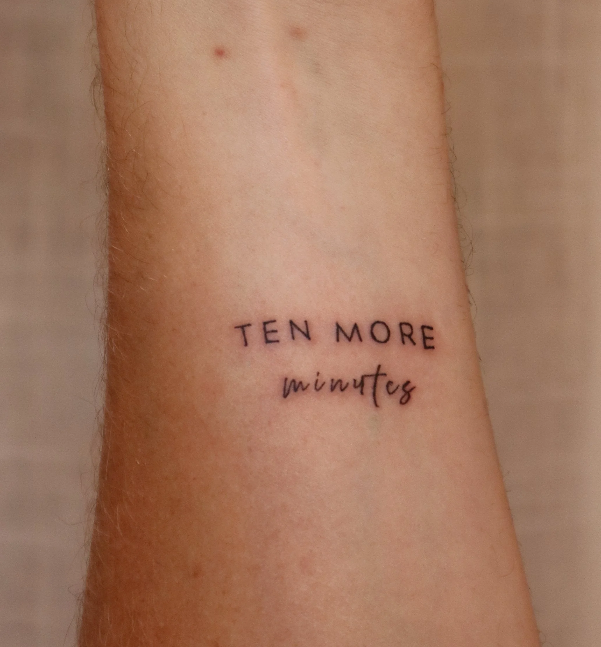 Tattoo on skin that says 'TEN MORE minutes' in black ink.