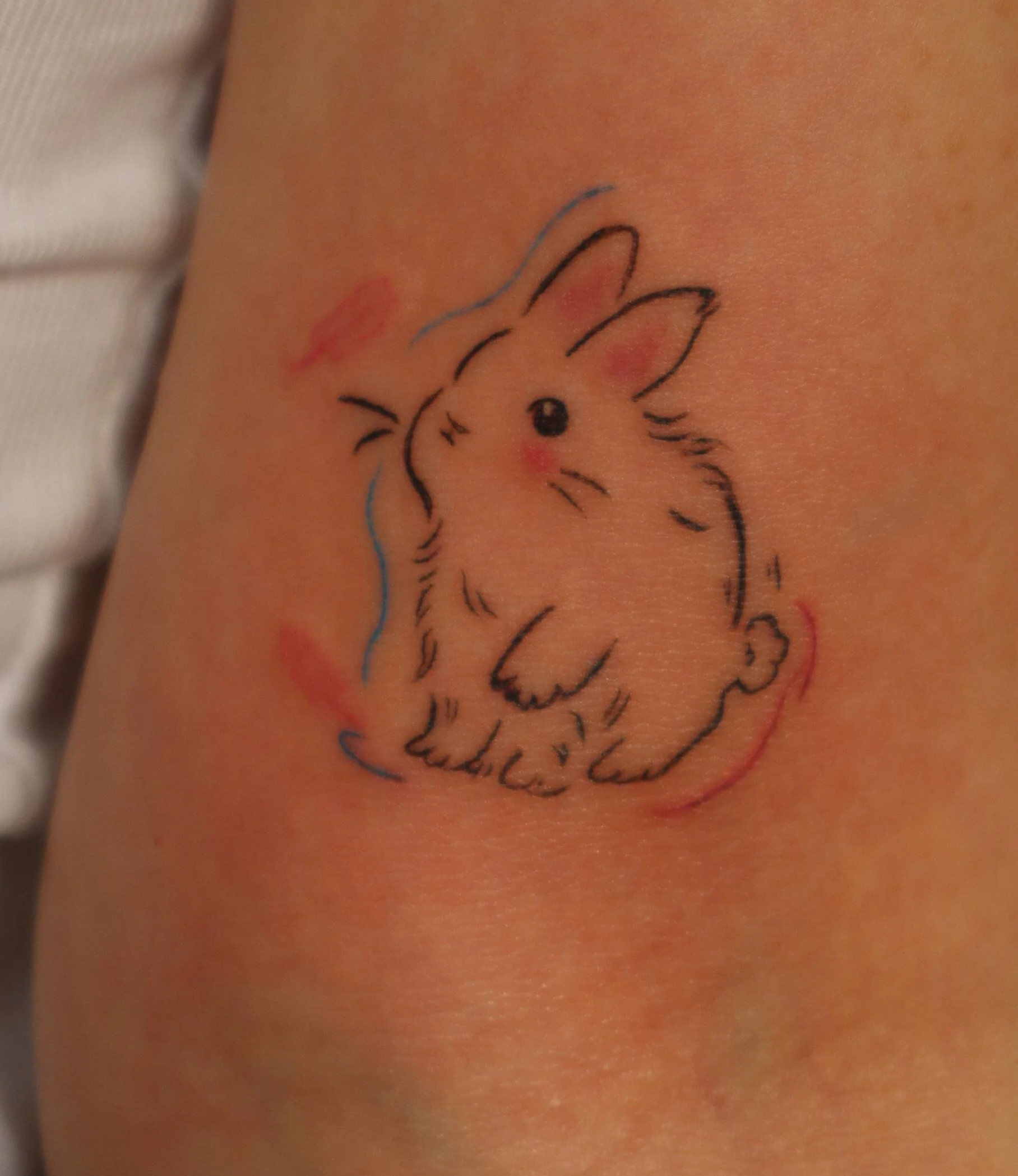 A colorful tattoo of a bunny with a crown, drawn with simple black lines, on a person's skin.