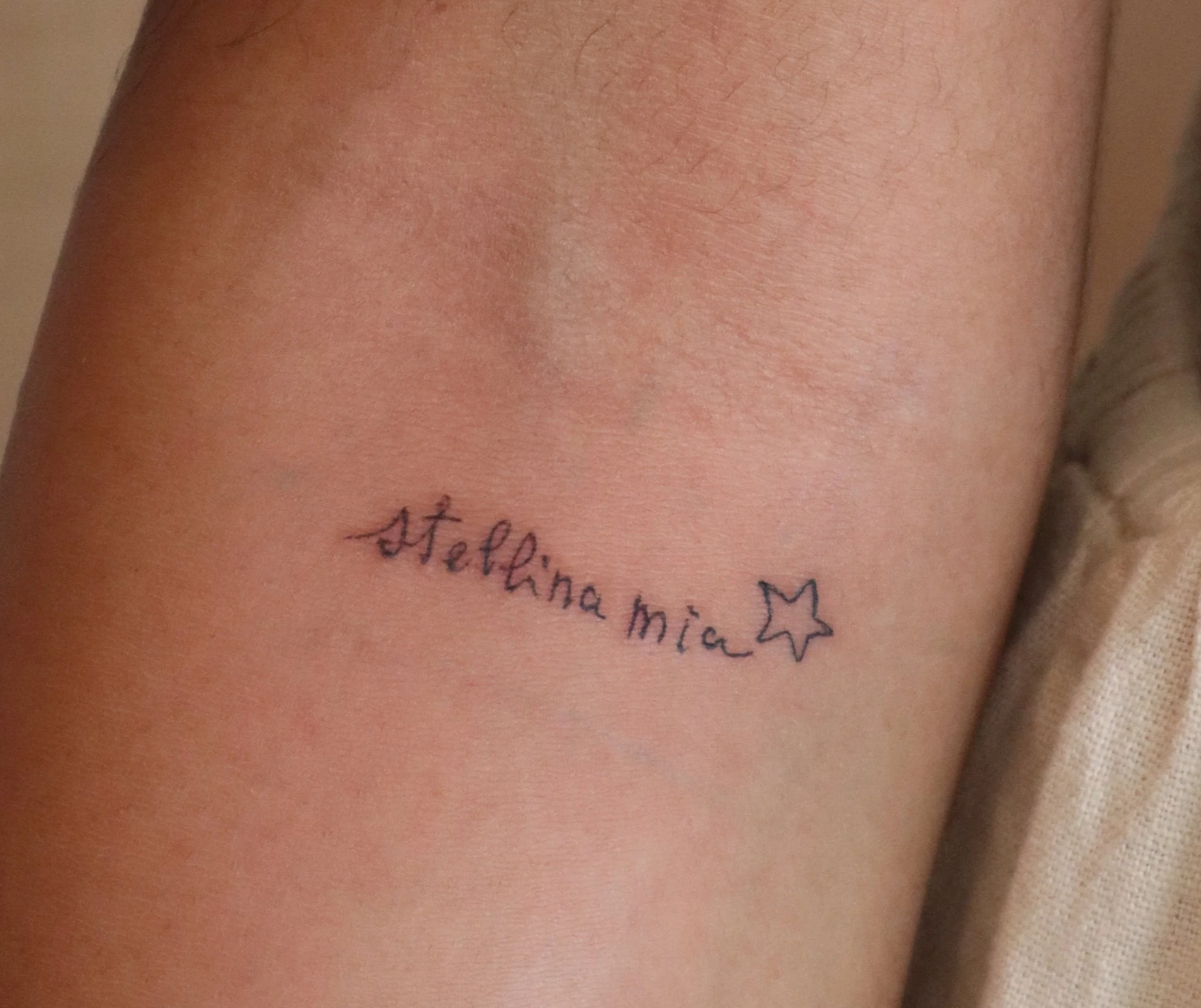 Tattoo on upper arm with the words ‘Stellina Mia’ and a small star outline.