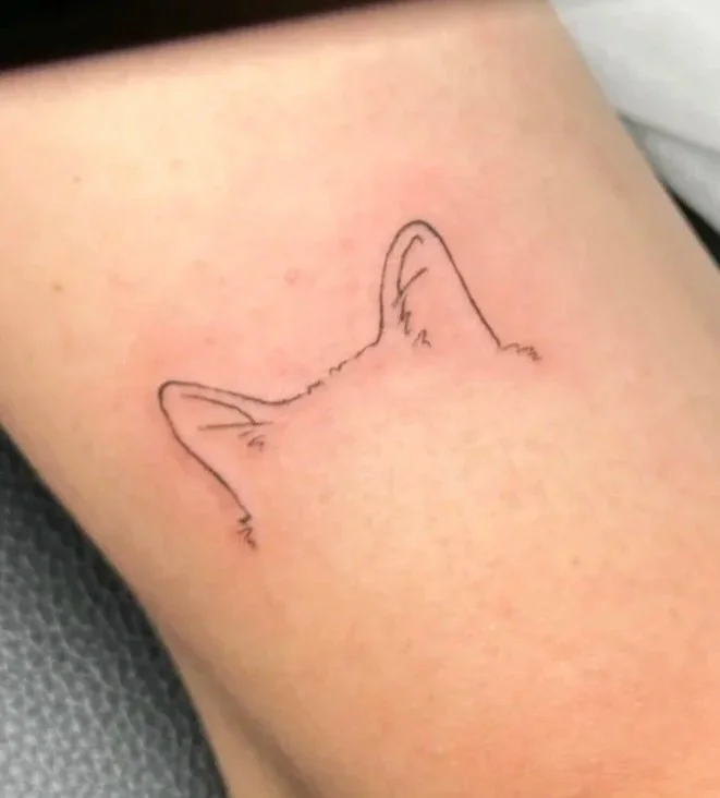Minimalist tattoo outline of a cat's ears on skin.