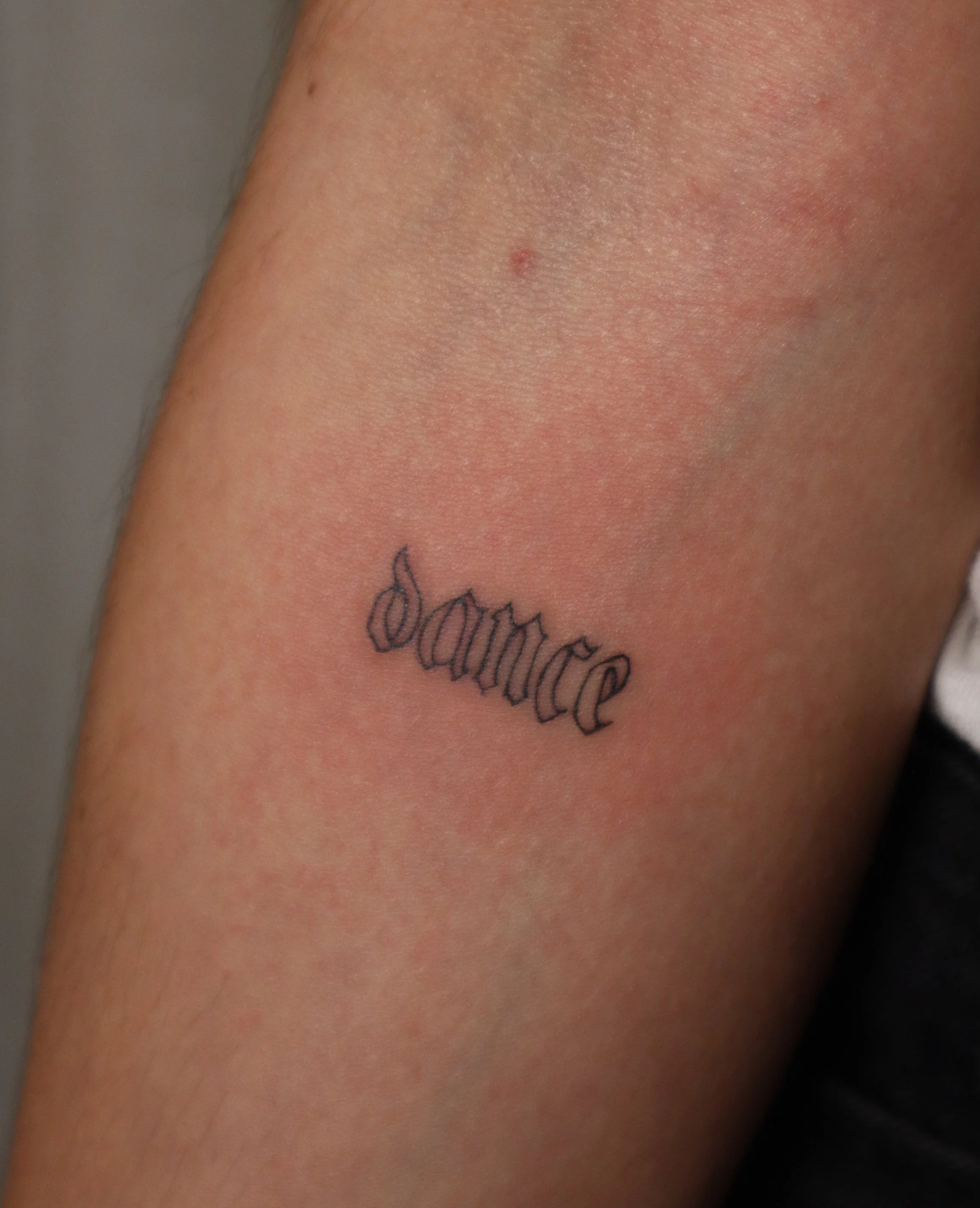 Tattoo of the word 'dare' in black Gothic script on a person's upper arm near the shoulder.
