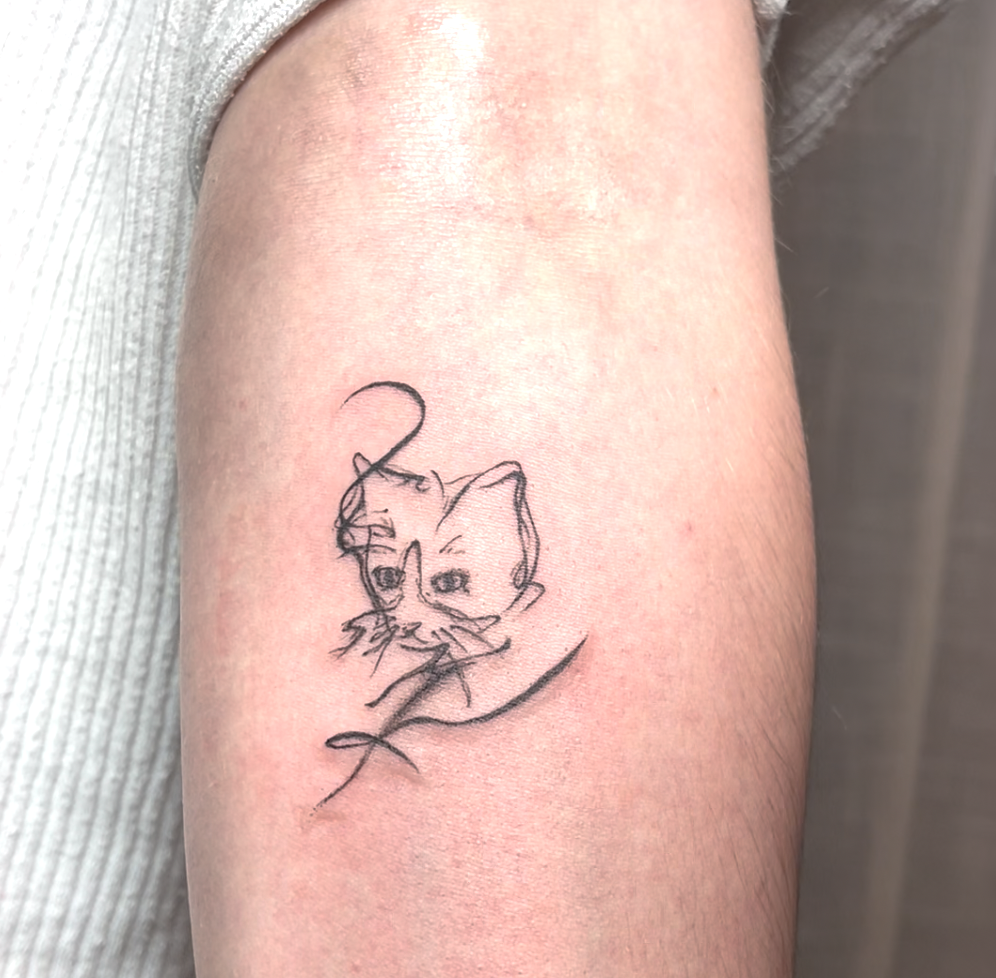 A tattoo of a cat's face drawn with minimalist, sketchy lines on a person's arm.
