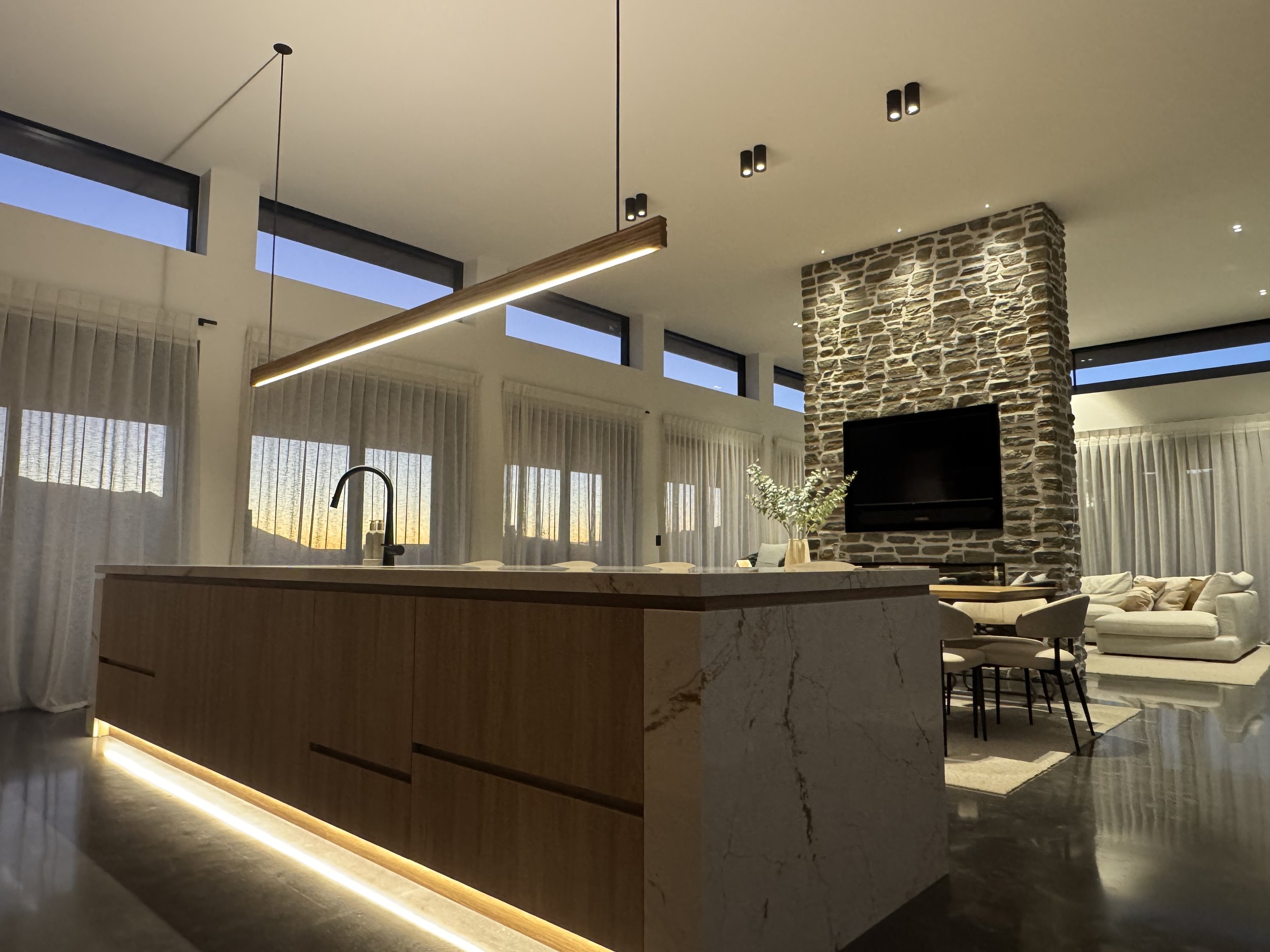 Image showing architectural kitchen and dinning. High ceilings glowing lights, stone TV tower and wooden pendant