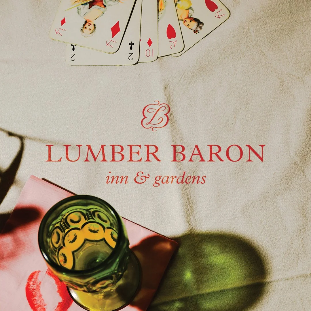 Tablecloth with the logo and name of Lumber Baron Inn & Gardens, a glass with a beverage, and playing cards on a table.