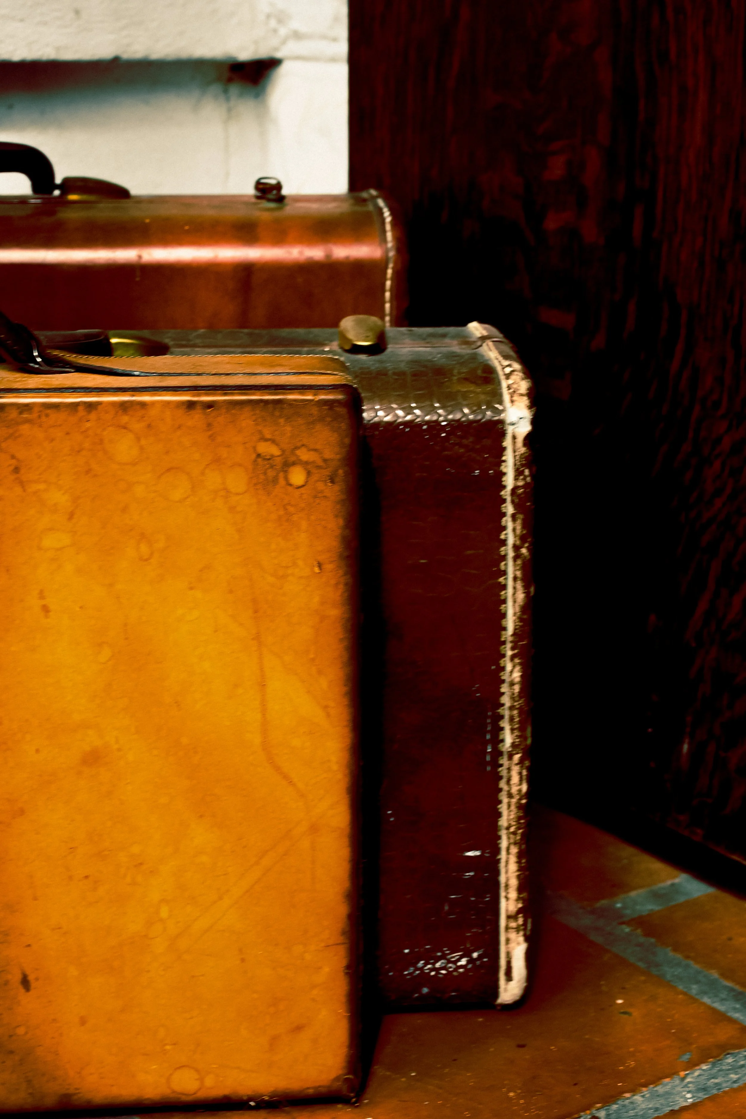 Close-up of vintage brown and dark brown suitcases stacked on the floor against a wall.