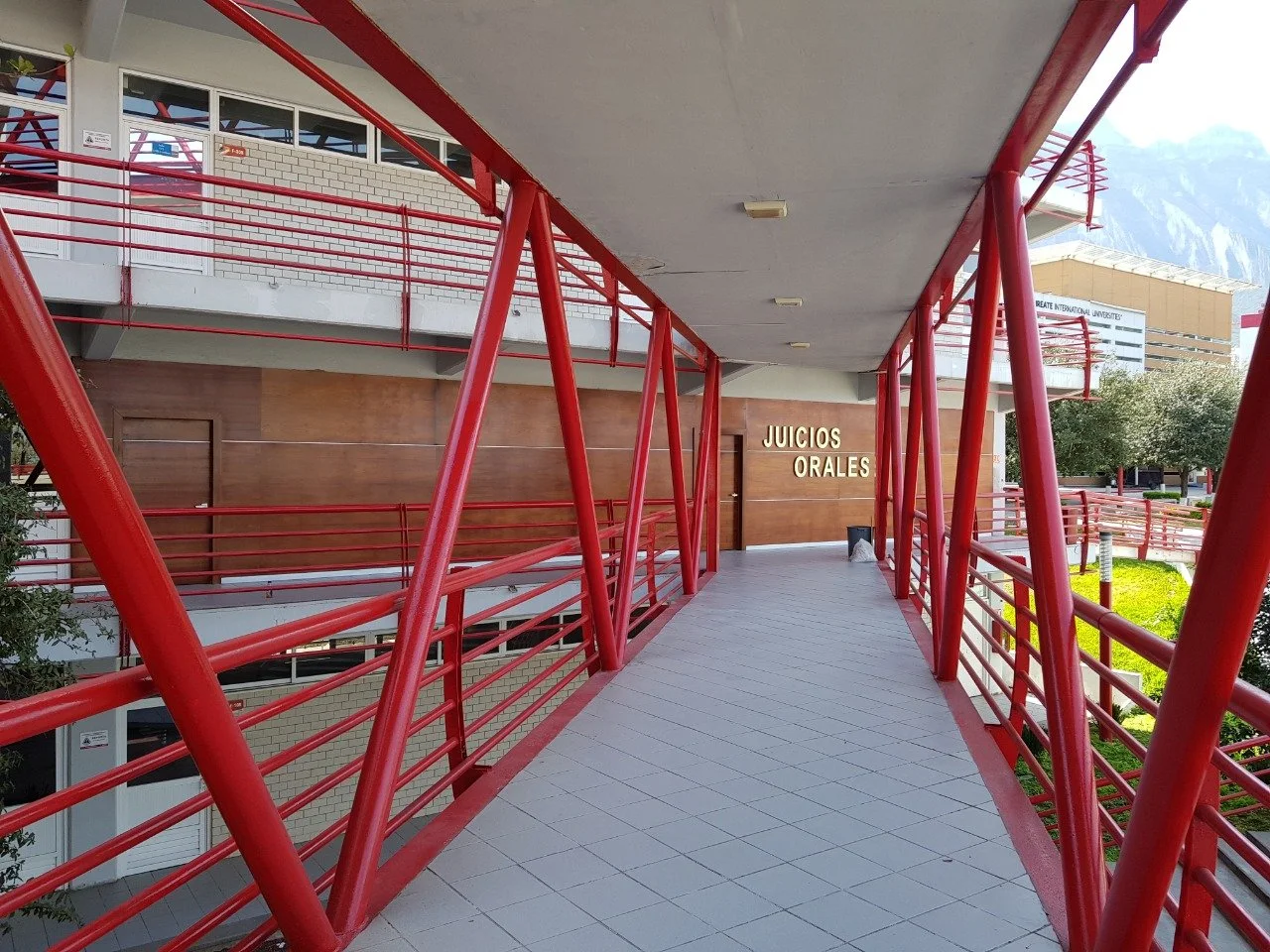 Pasarela con barandillas rojas en un edificio de juzgados llamado 'Juicios Orales'.