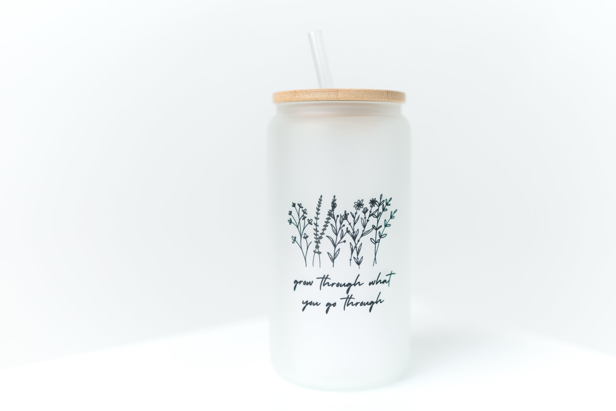 Glass jar with wooden lid and straw, featuring floral illustrations and the text 'grow through what you go through'.