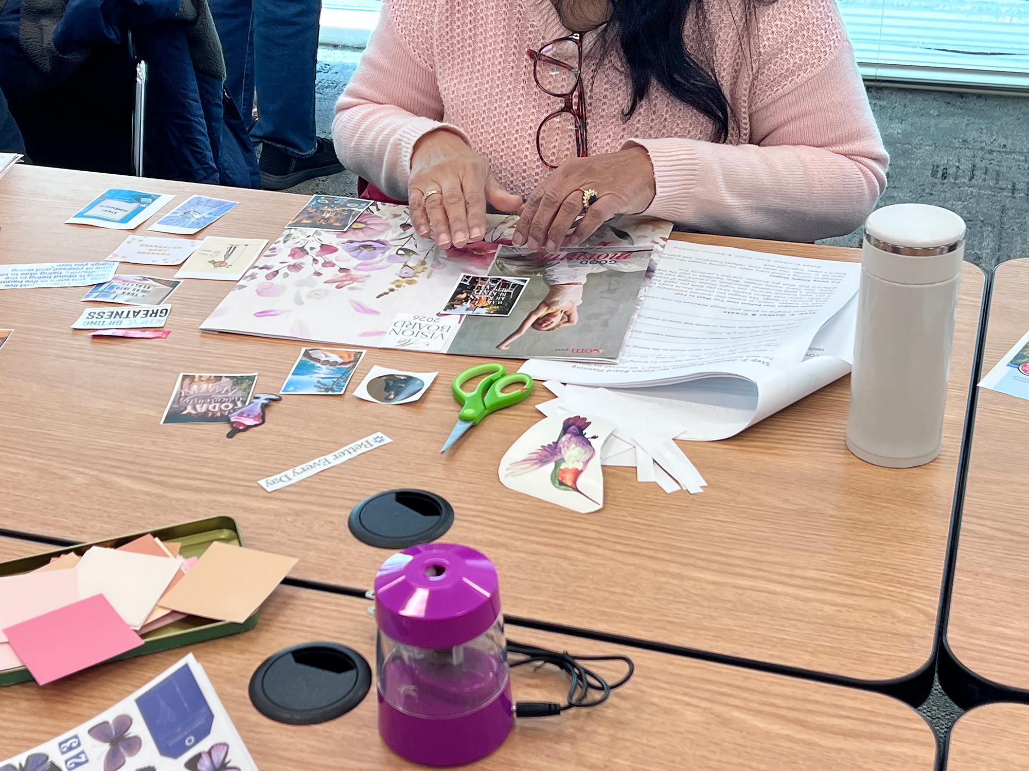 Woman's hands arranging cut images and words on a vision board during an expressive arts workshop