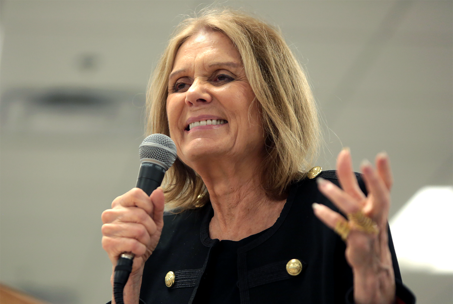 Gloria Steinem smiling while holding up a microphone to her mouth.