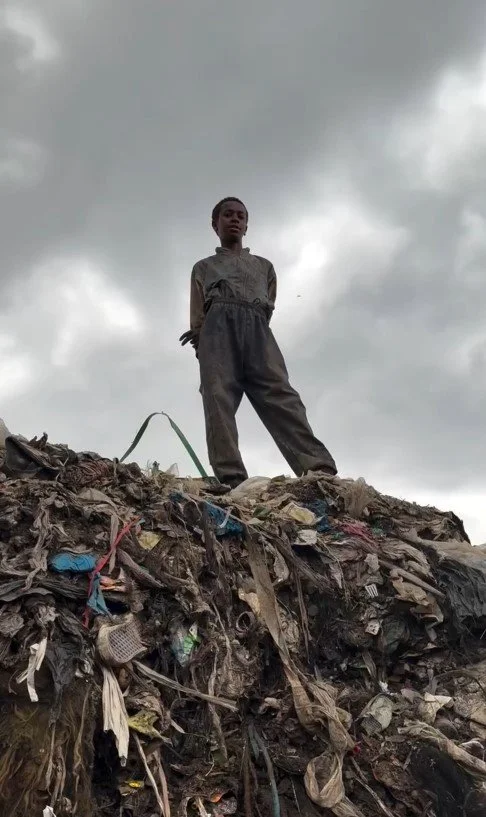 Person standing on a pile of trash under a cloudy sky.