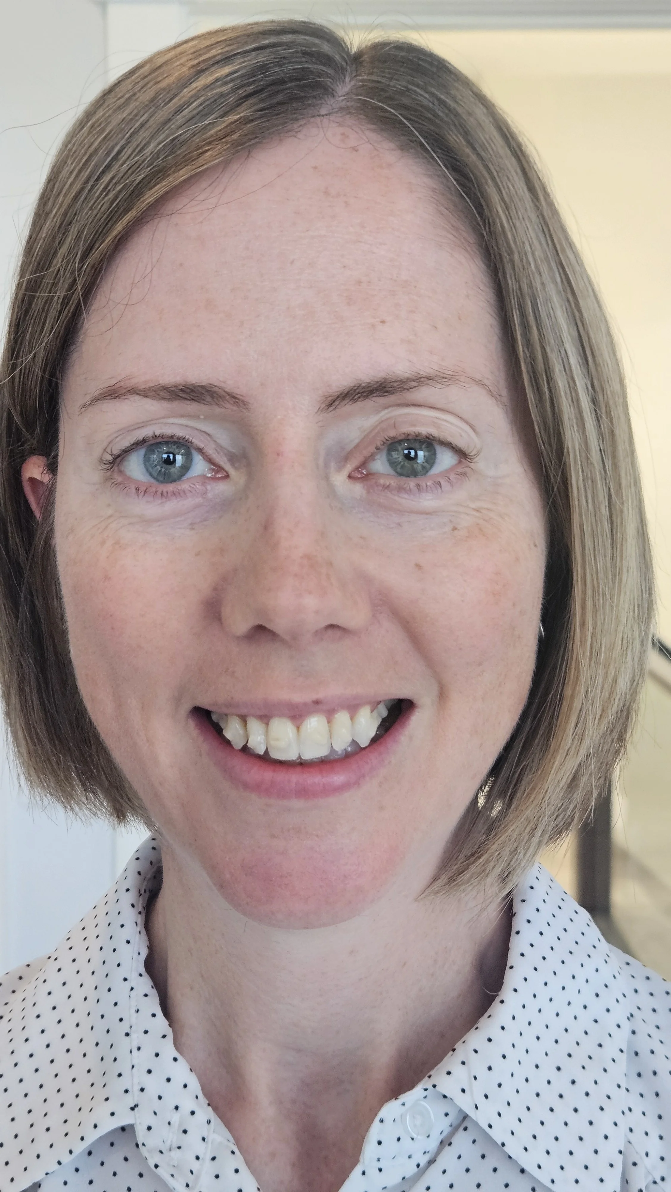Women with a blonde bob in a white collared shirt smiling