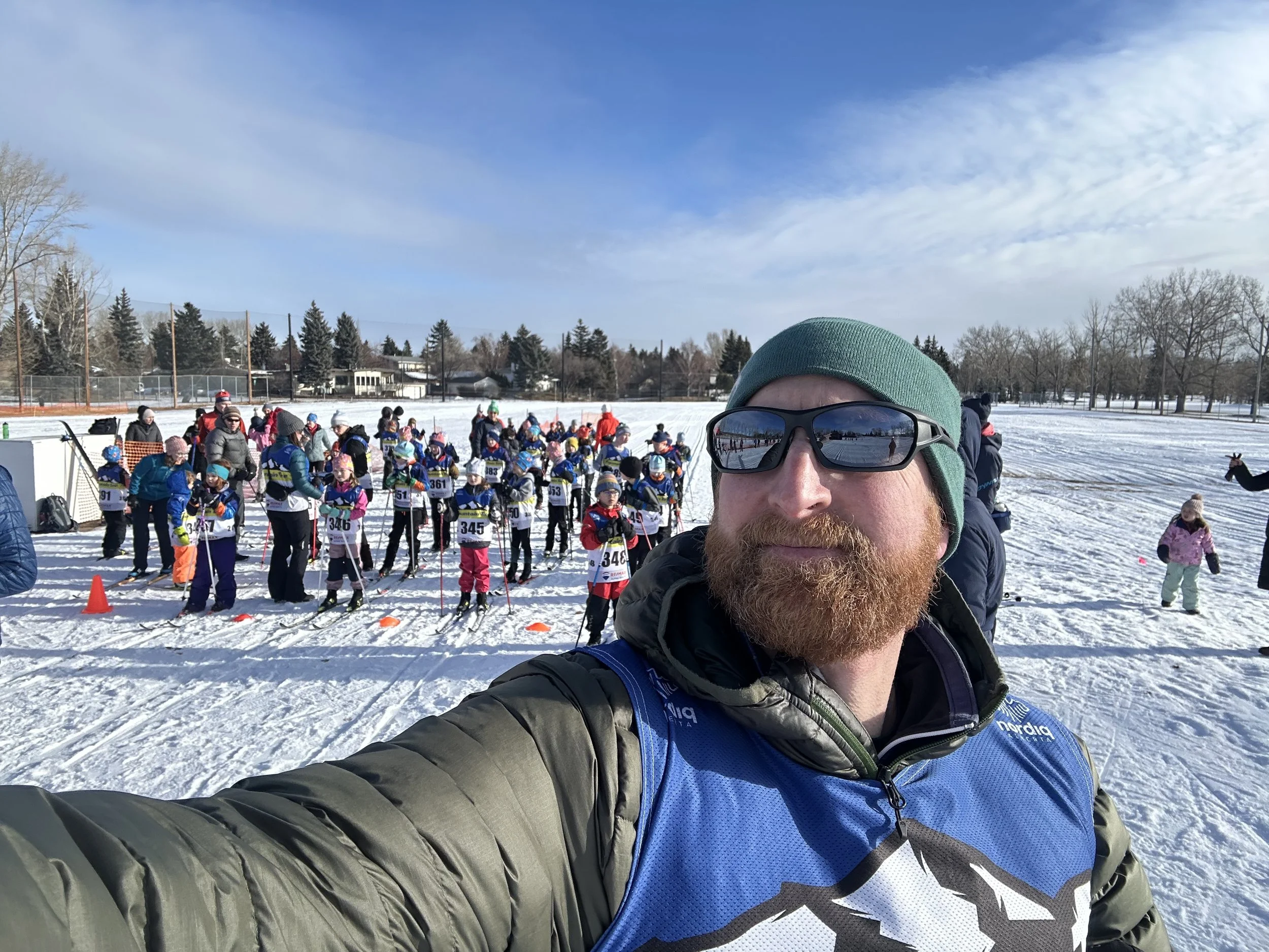 Person outdoors in a snowy setting holding a wooden beam, wearing a blue and black jacket with orange and white accents.