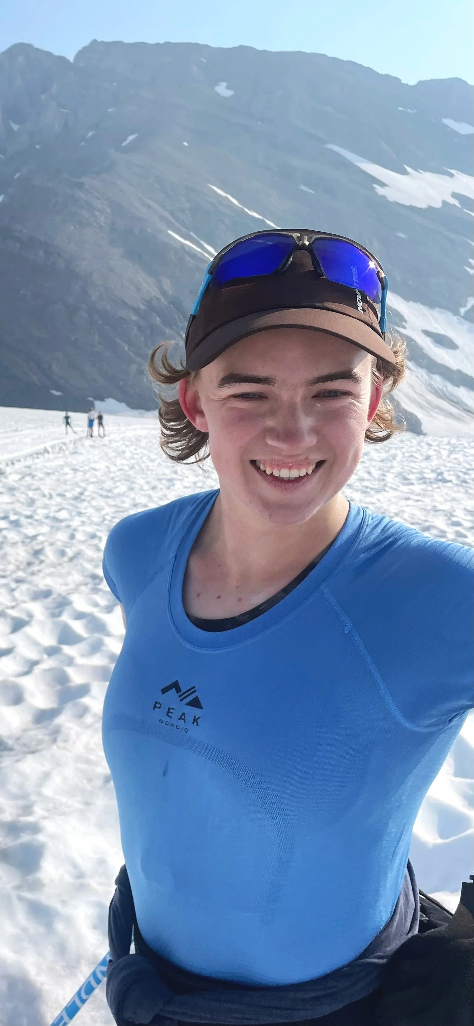 Person in ski gear smiling with thumbs up in snowy mountain landscape.