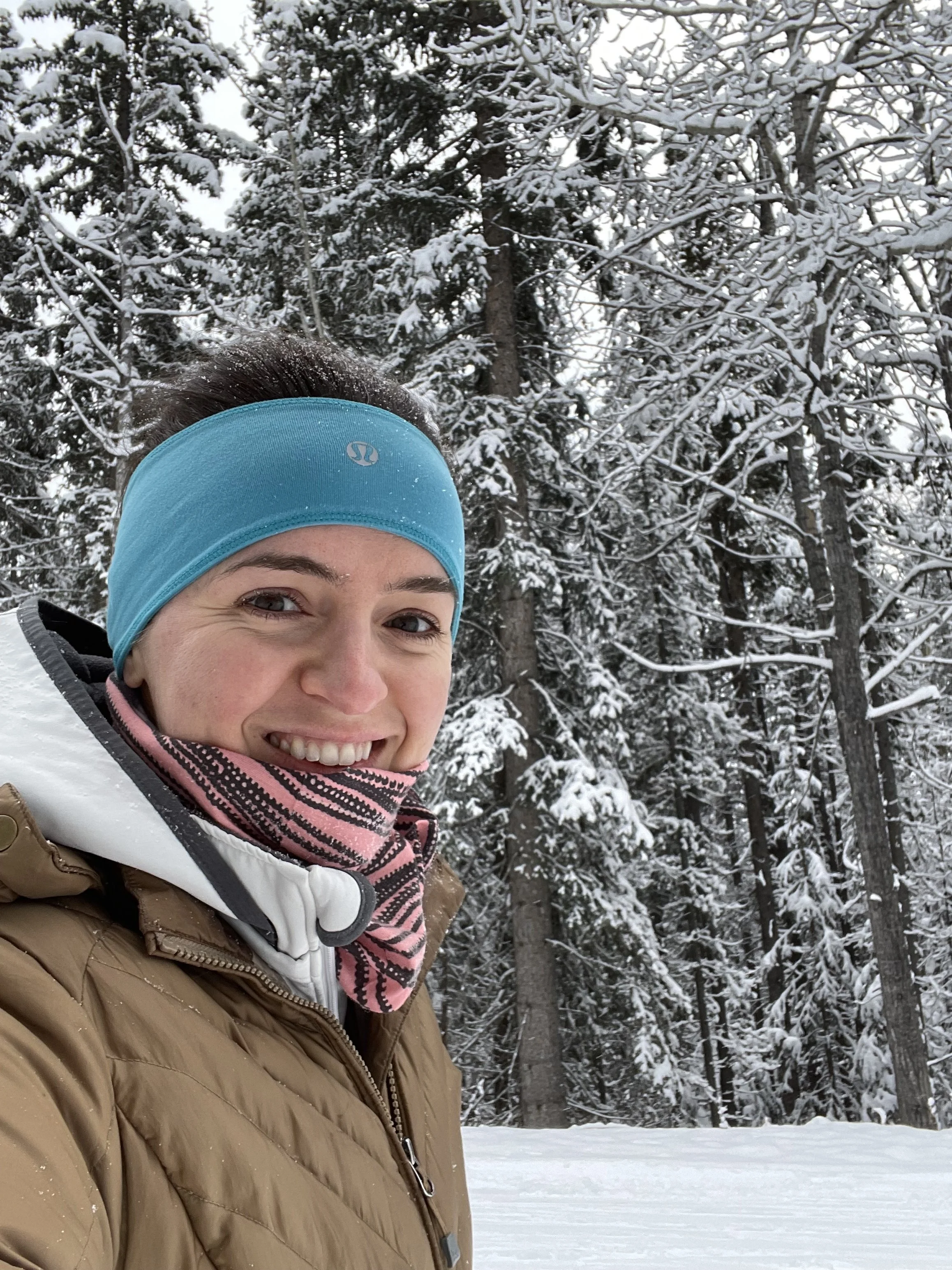 Woman in a headband and winter coat smiling in the snow