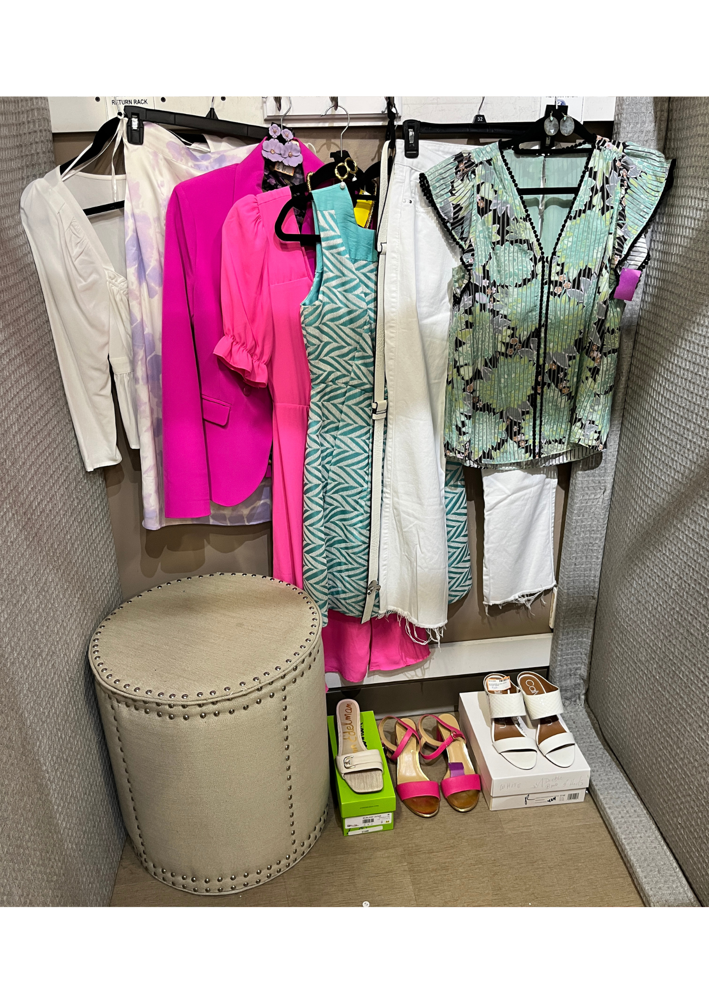 Clothing and footwear on display in a fitting room, including colorful dresses, blouses, pants, and high-heeled shoes.