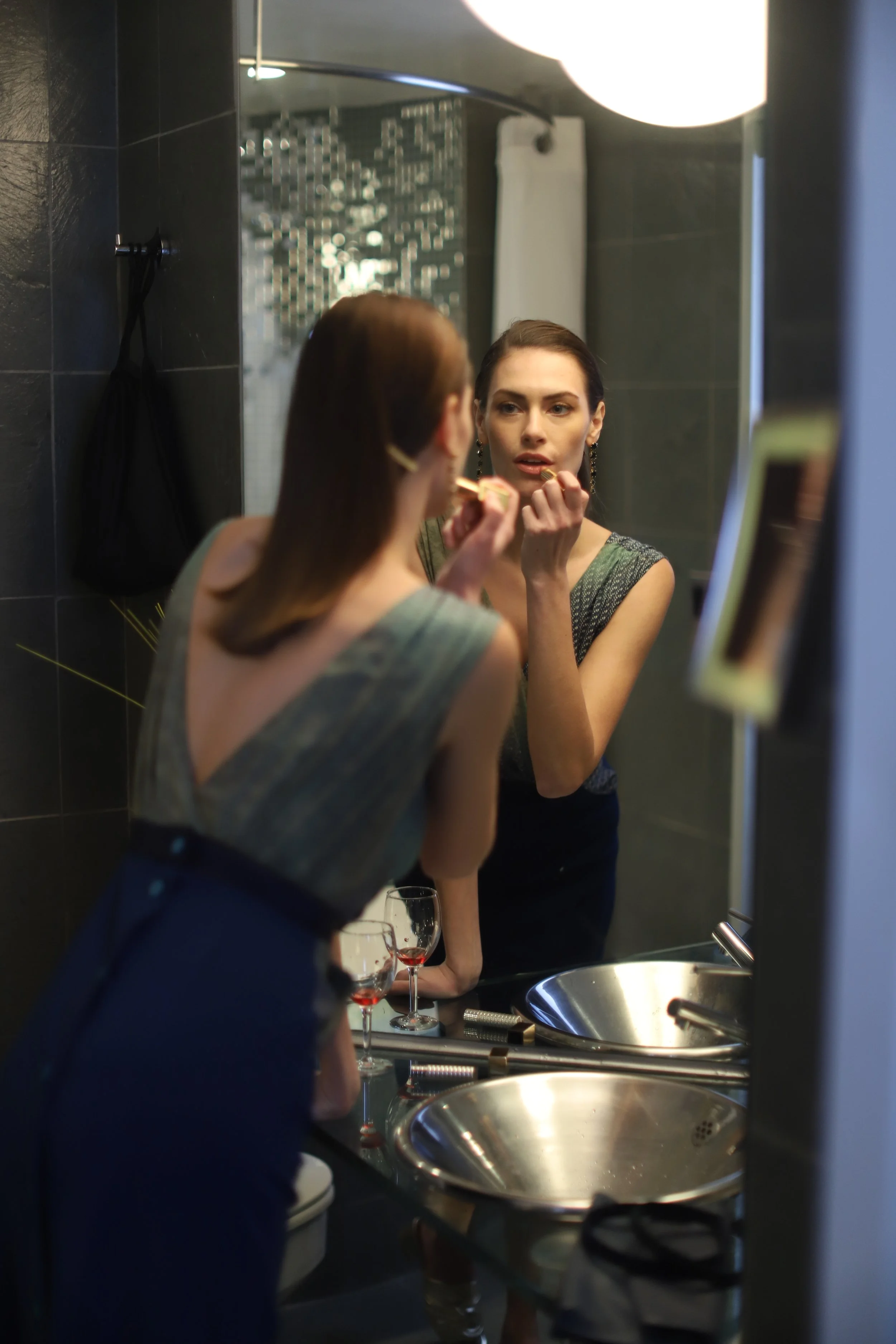 Model applying lipstick in the bathroom mirror reflection while wearing a Dreams in an Armoire Anita dress.