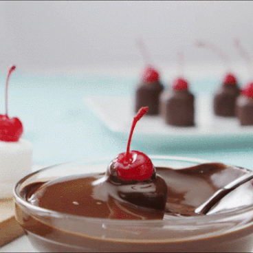 Cherry-topped marshmallow lifting out of melted chocolate.