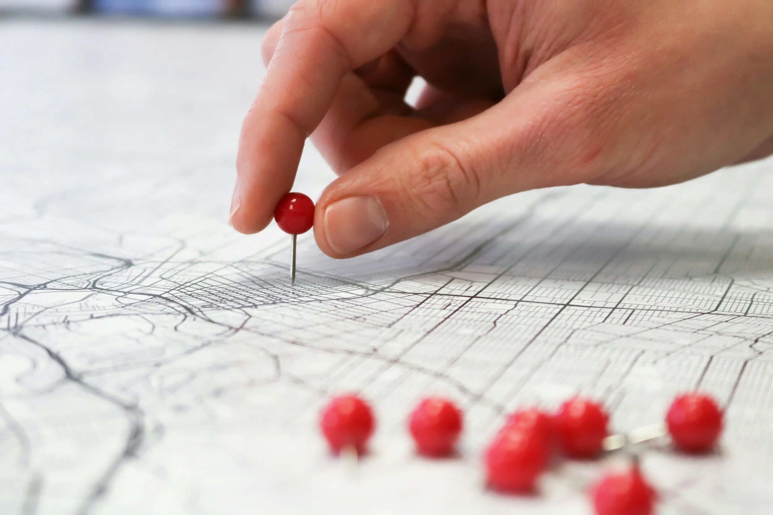A person uses a red pushpin to mark a location on a map with streets and a grid pattern.