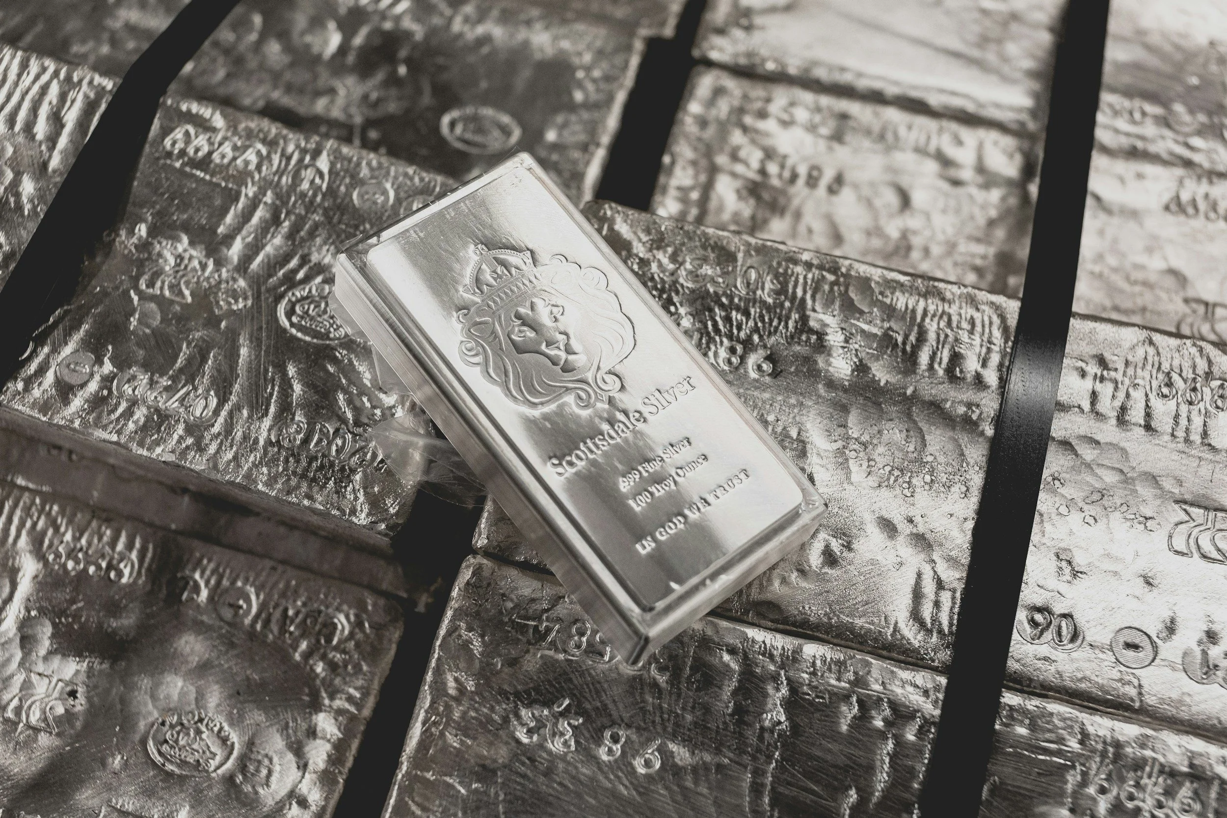 Silver bars stacked together with a plastic-wrapped silver bar placed at the center, engraved with a lion's head and text indicating it's Scottish silver of 999 purity.