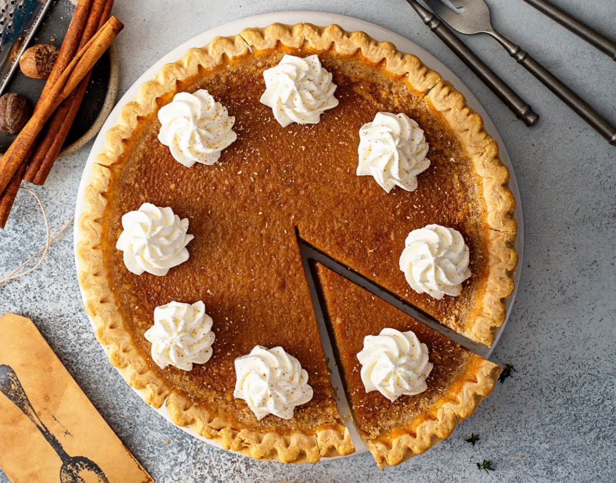 A caramelized pumpkin pie topped with whipped cream dollops, with a slice missing, on a round white plate.